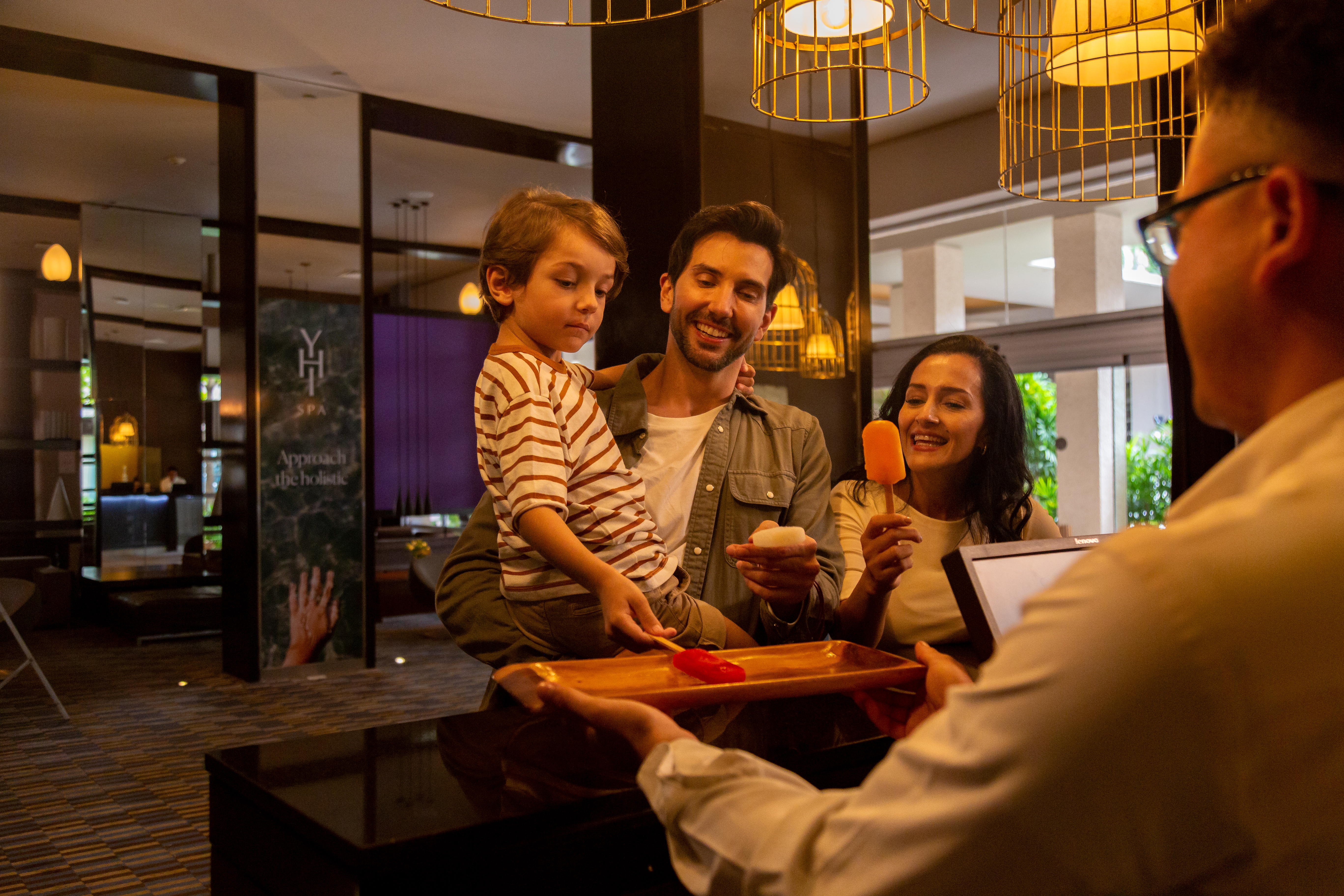 Family receiving welcome popsicles at hotel reception desk.