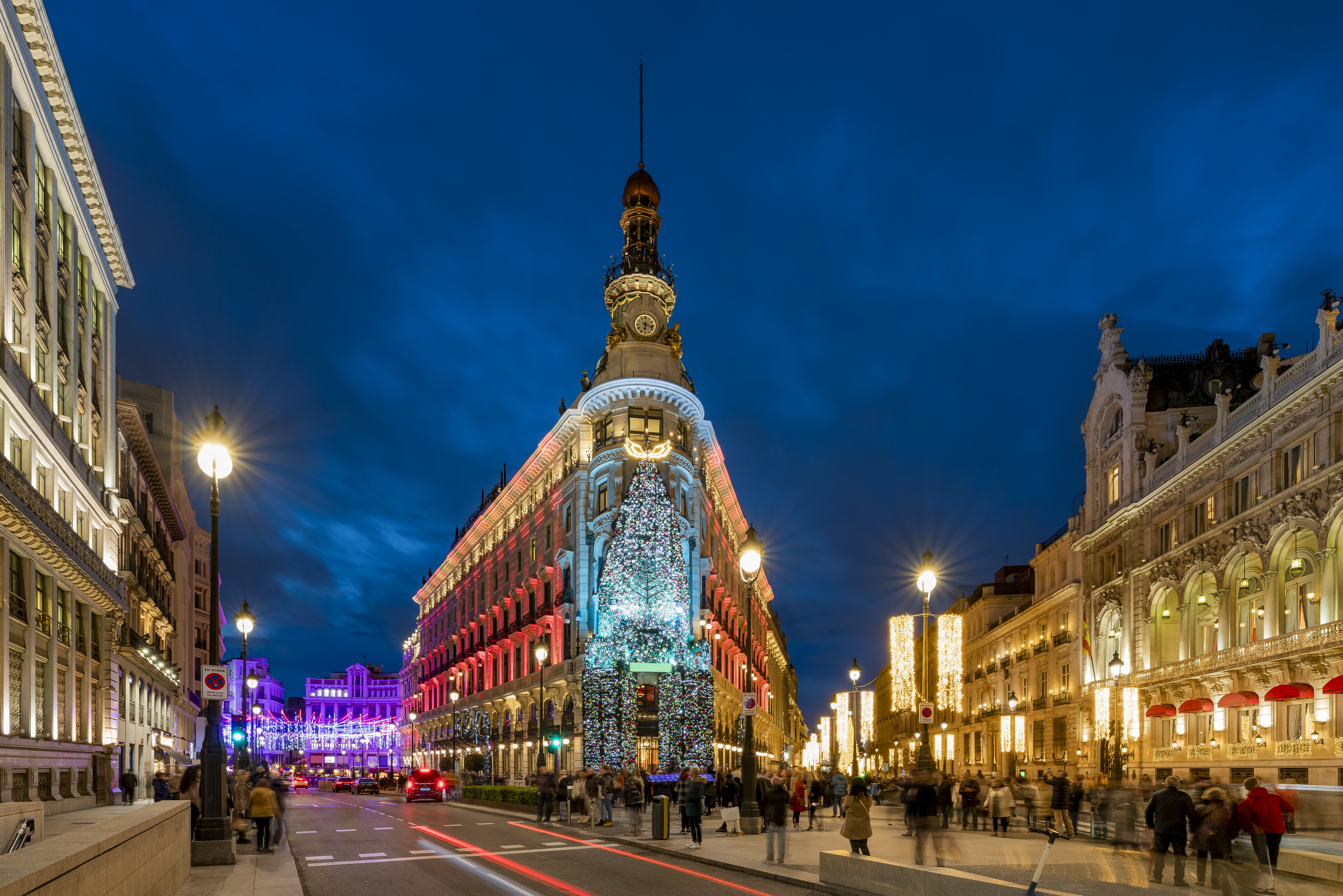 A busy city street filled with lights and crowds of people strolling by.