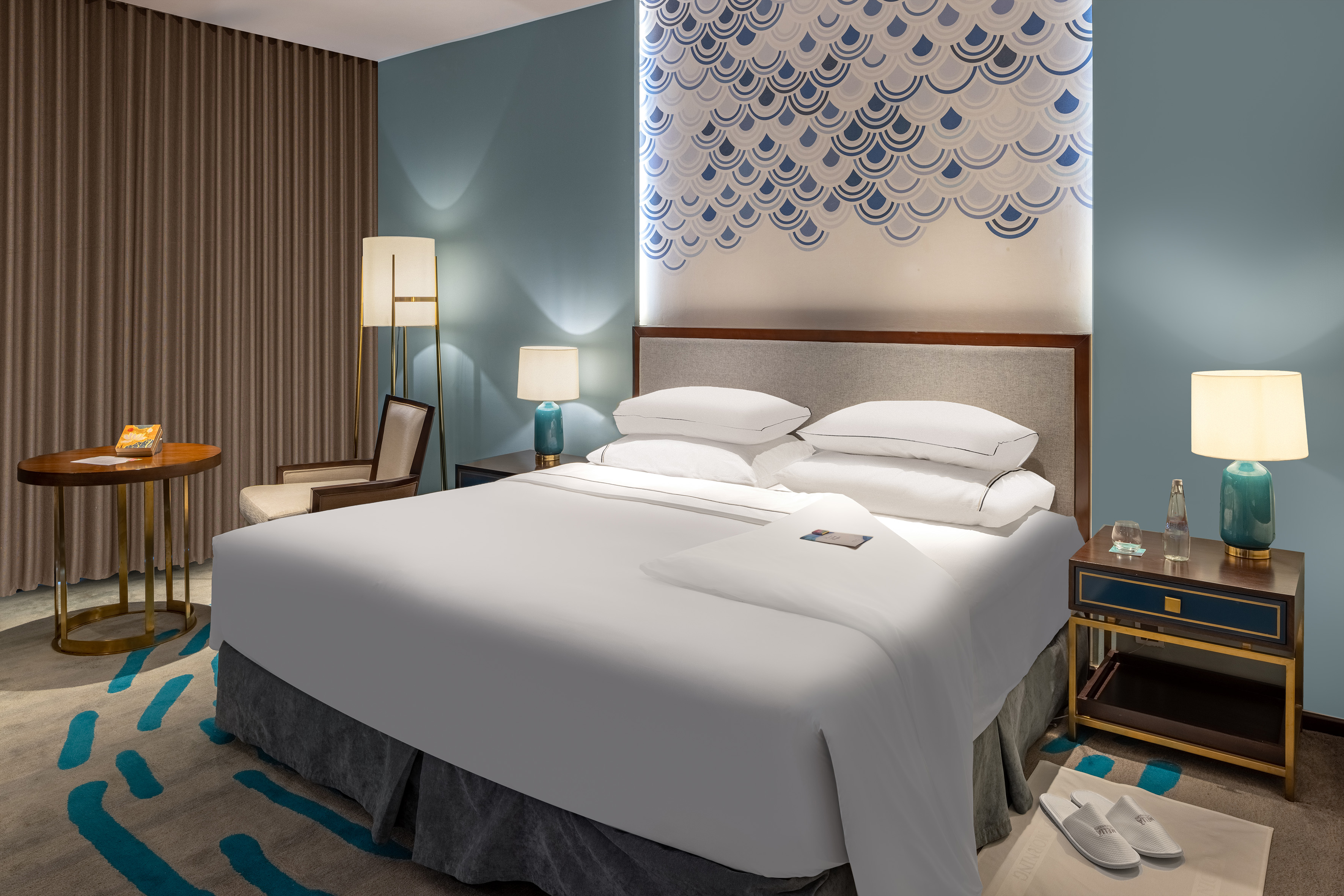 Stylish hotel bedroom with blue patterned wall, large bed, and cozy decor.