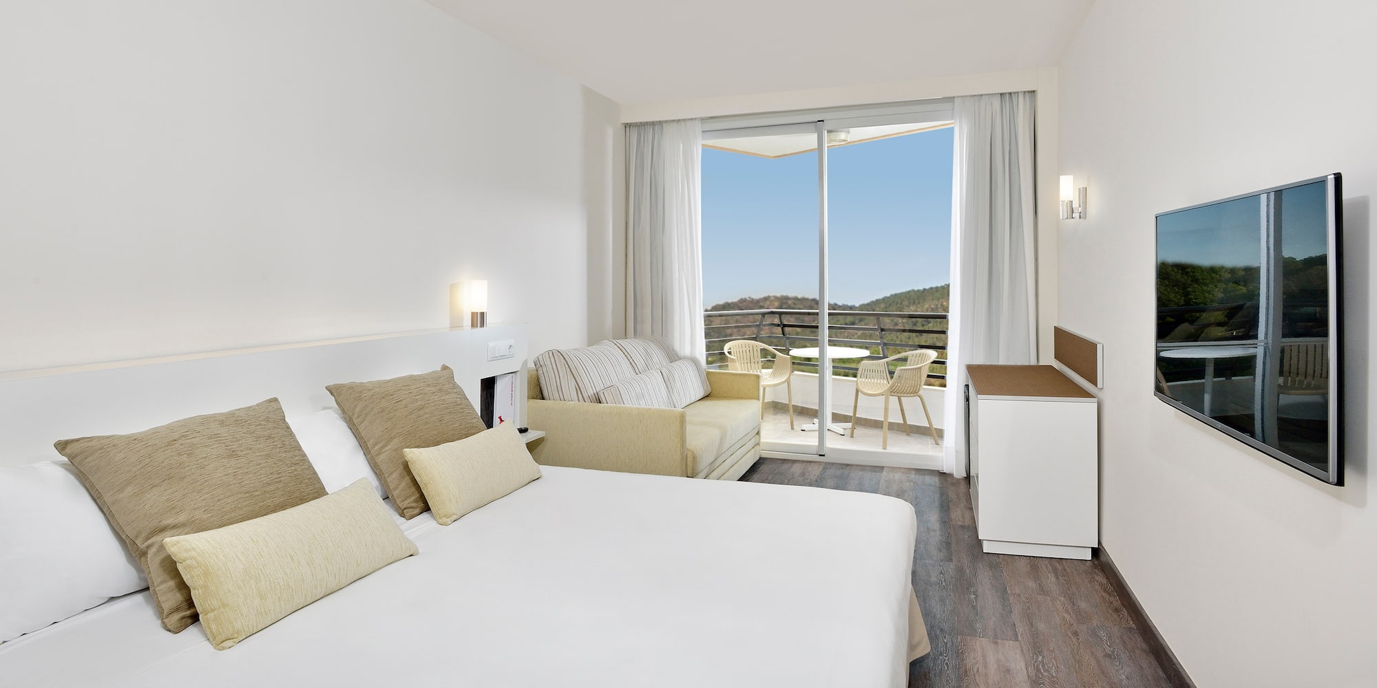 Modern hotel room with king bed, sofa, balcony, and scenic mountain view.