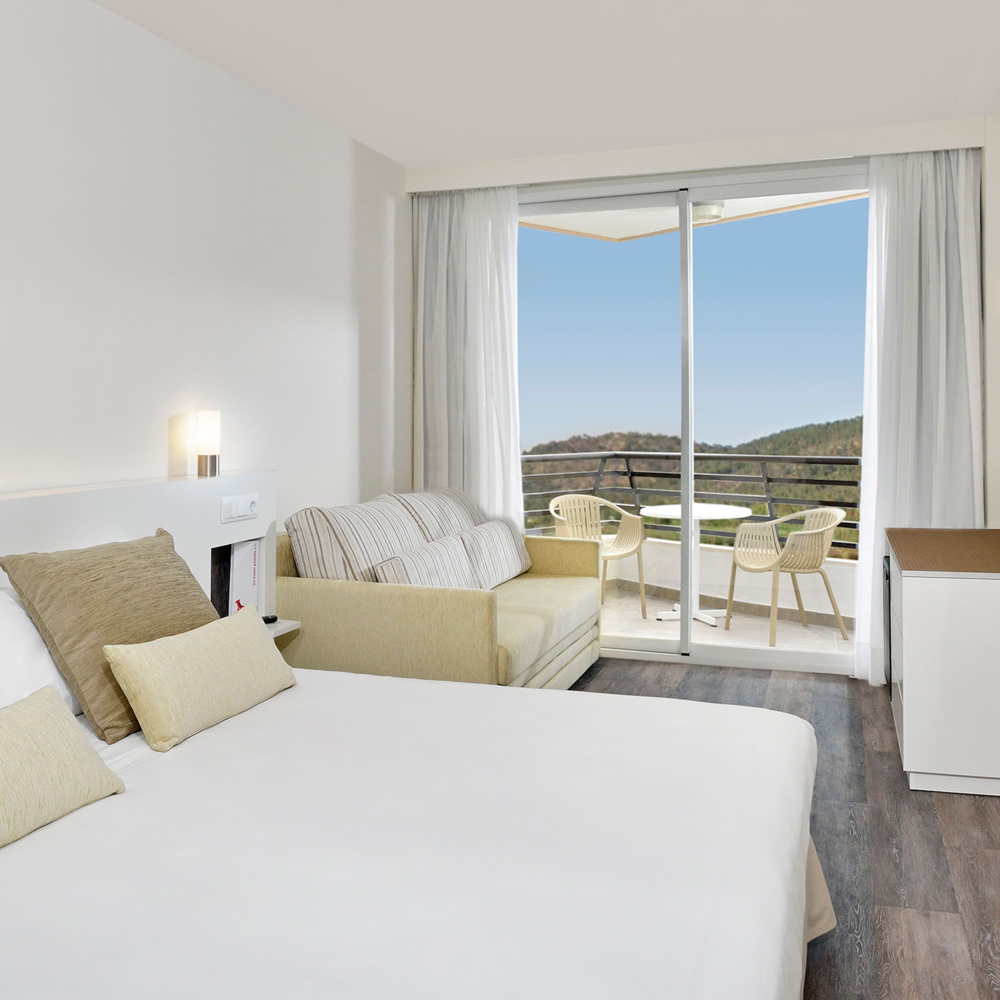 Modern hotel room with king bed, sofa, balcony, and scenic mountain view.