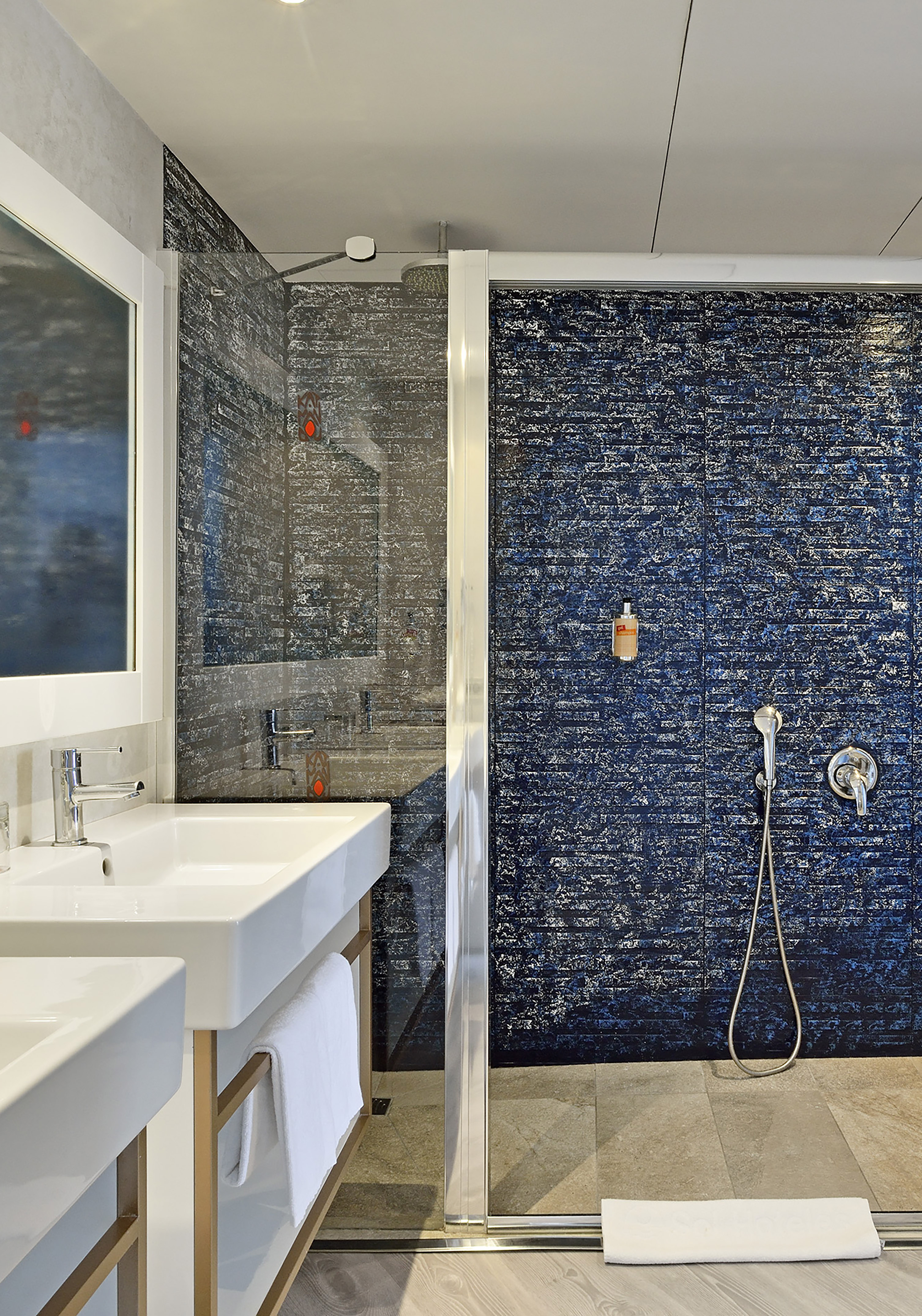 Hotel bathroom with dual sinks, modern shower, and striking blue tiled wall.