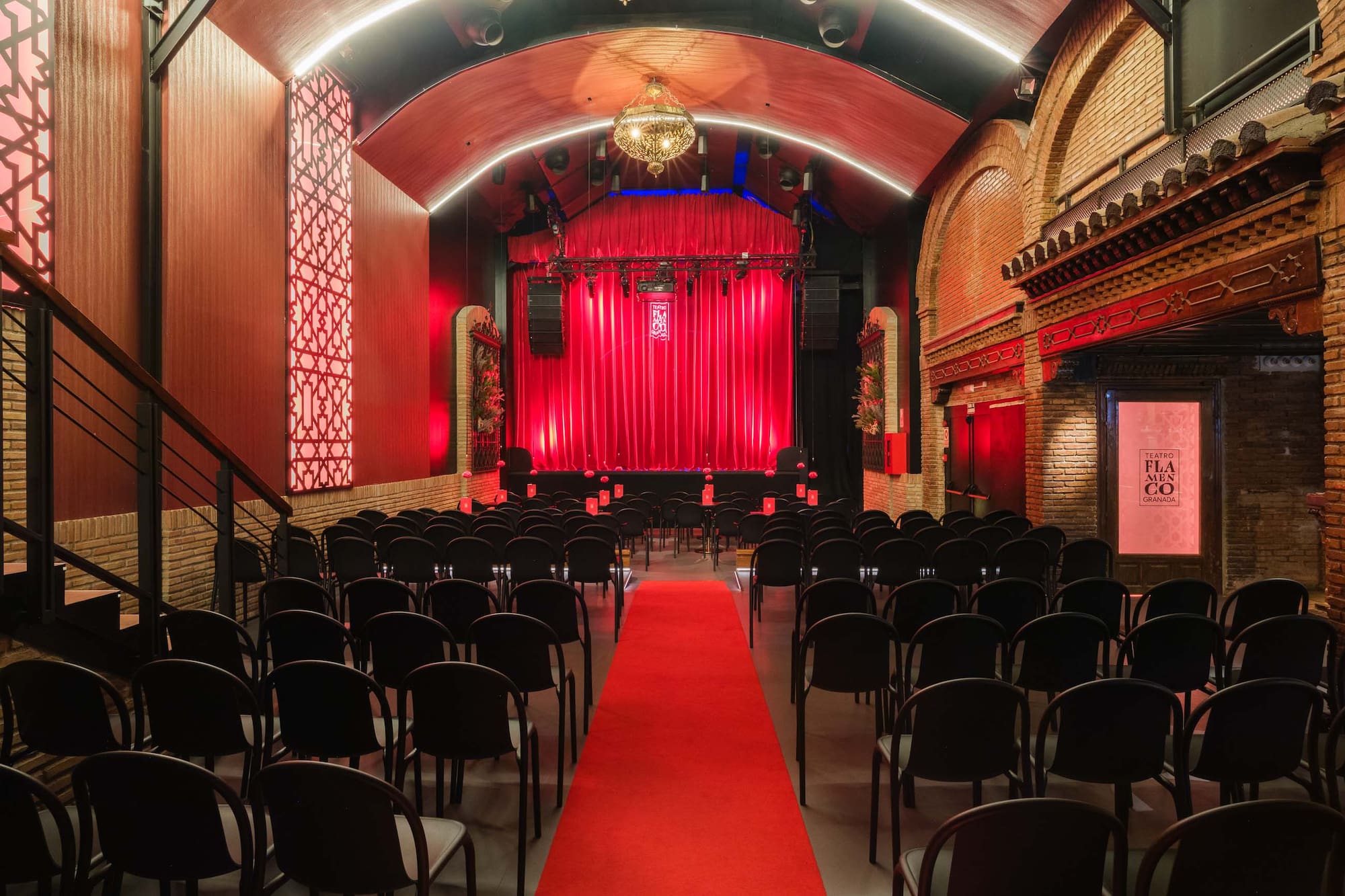 Sala de flamenco en Granada con butacas, alfombra roja y escenario iluminado.