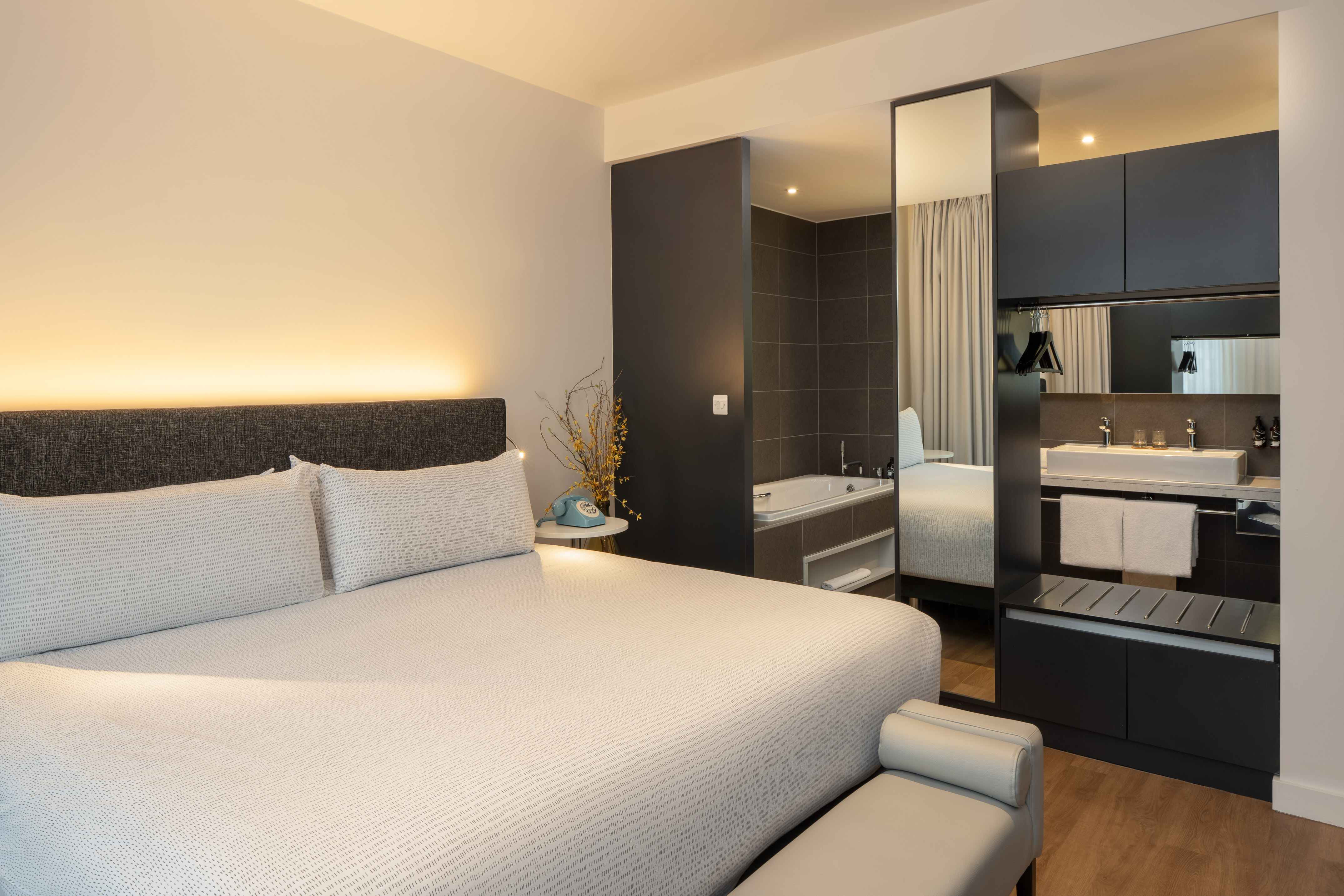 Modern hotel room with large bed, open-concept bathroom, tub, and vanity sink area.