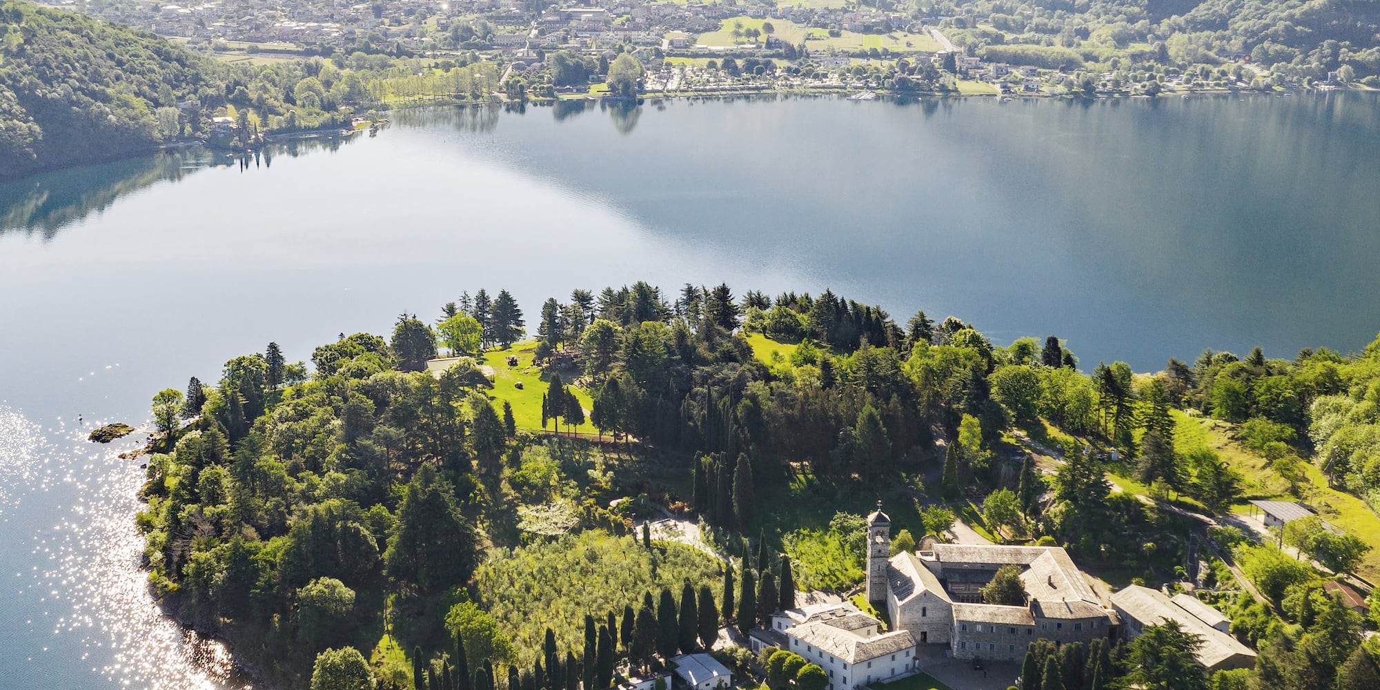 Aerial view of helicopter over lake, island monastery, and mountains.