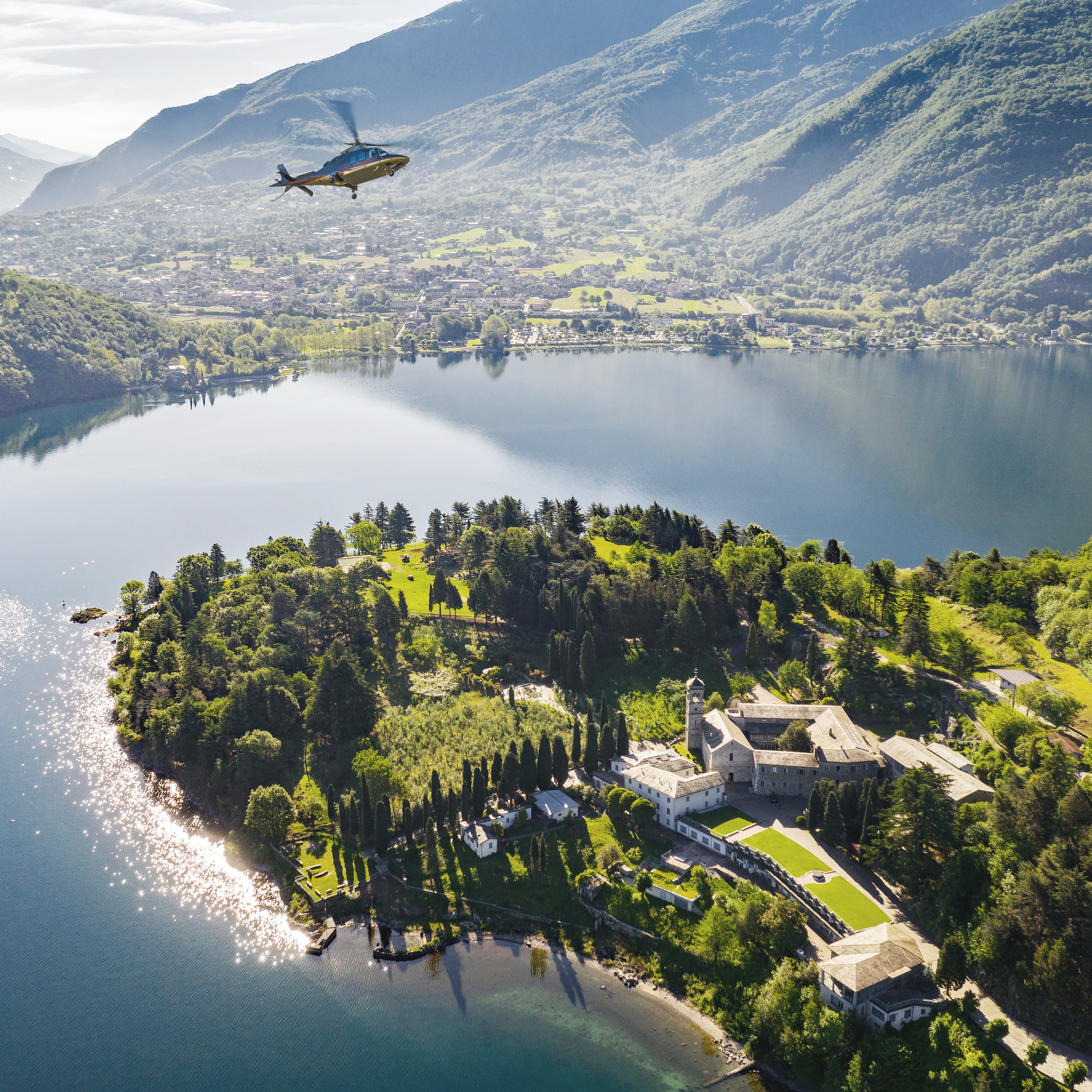 Aerial view of helicopter over lake, island monastery, and mountains.