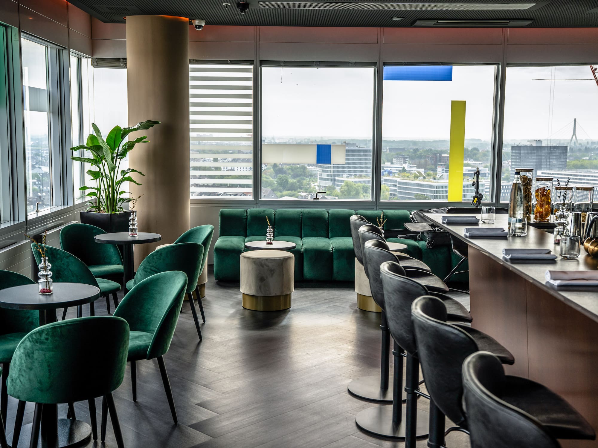 Modern sky lounge with green velvet seating, bar, and panoramic city views.