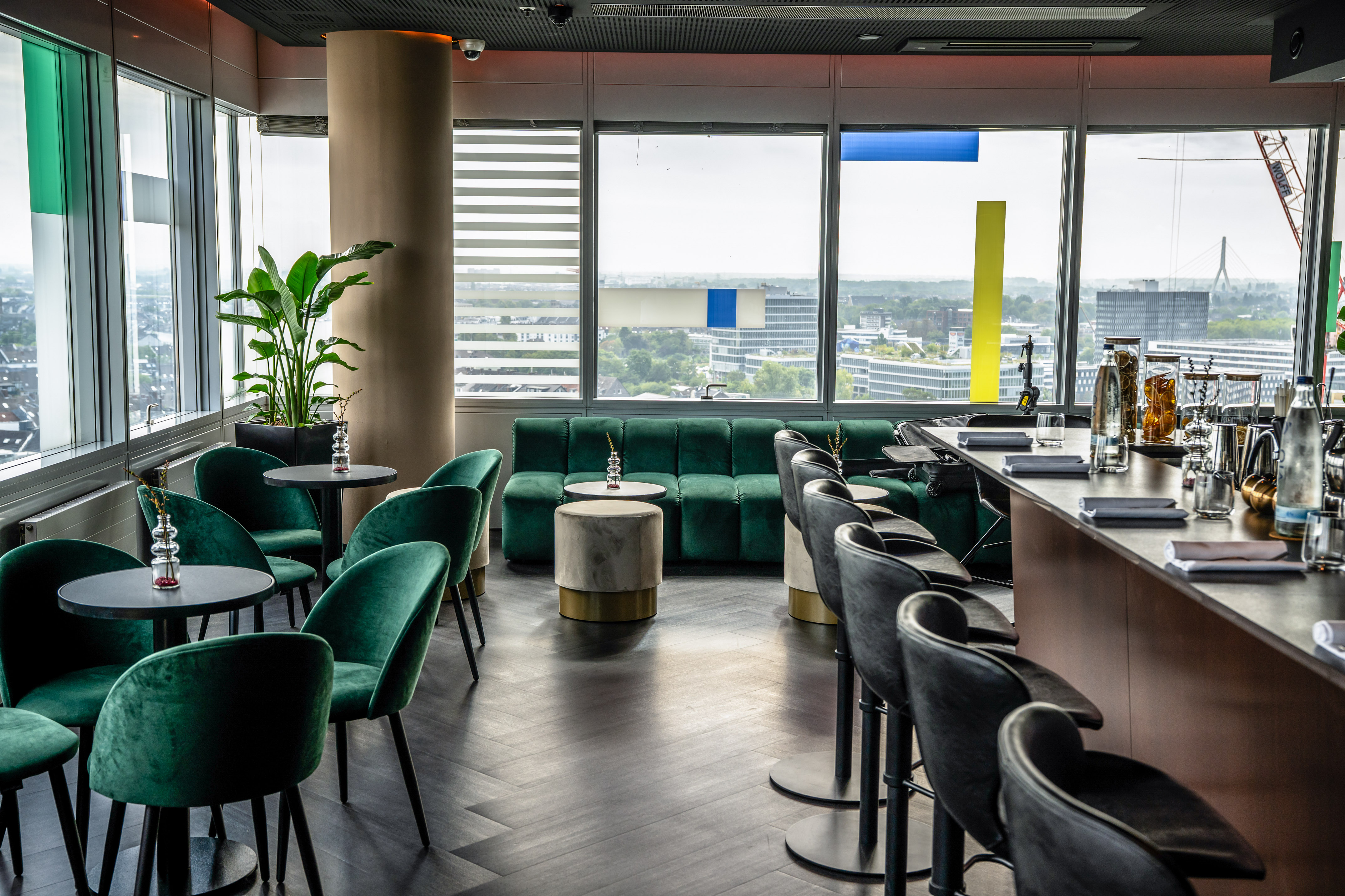 Modern sky lounge with green velvet seating, bar, and panoramic city views.