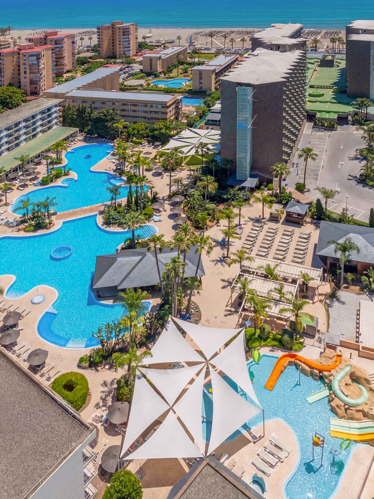 Beach resort aerial view: multiple pools, waterslides, hotels, ocean.