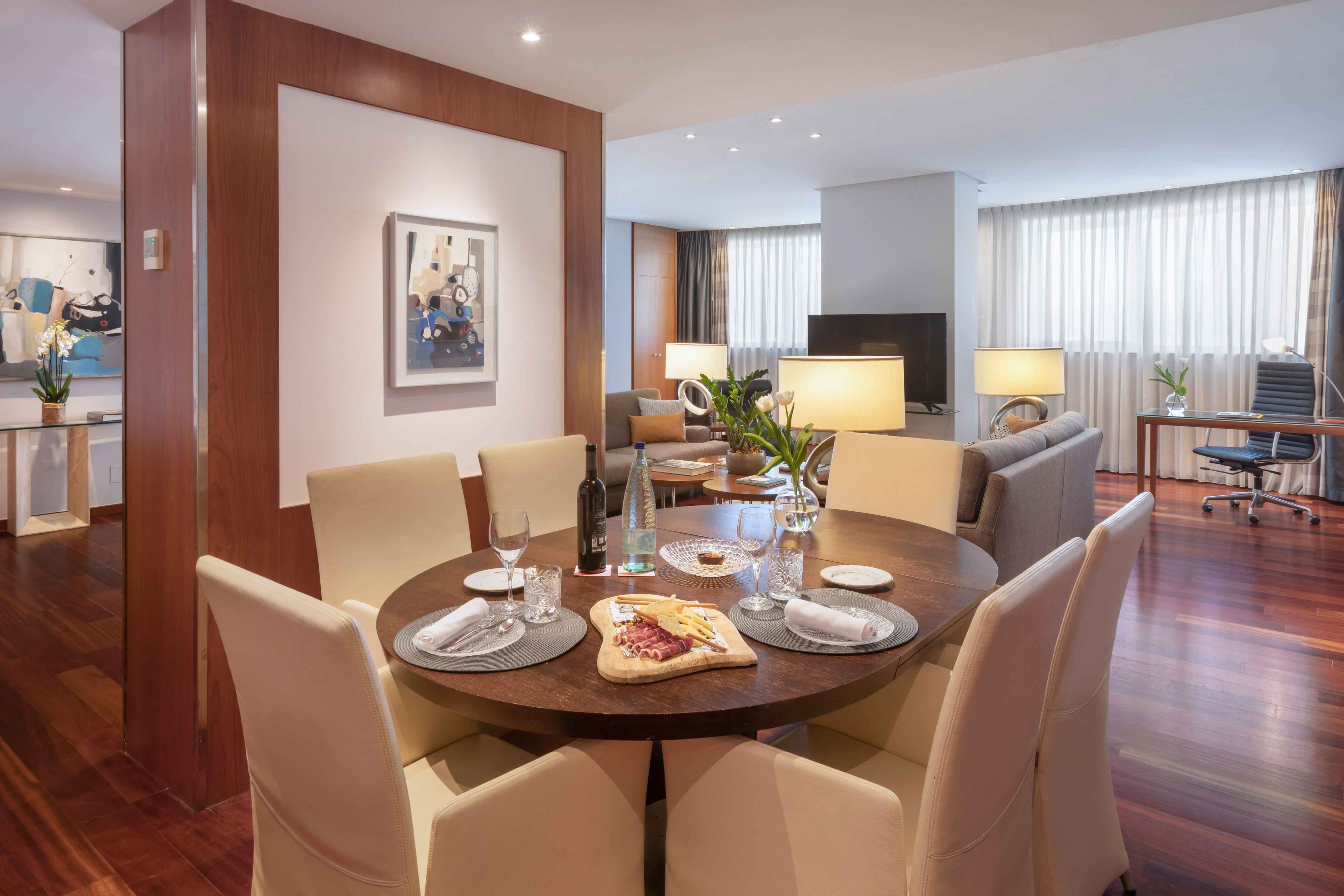 Modern dining table with charcuterie board, wine, in an open-plan living area.