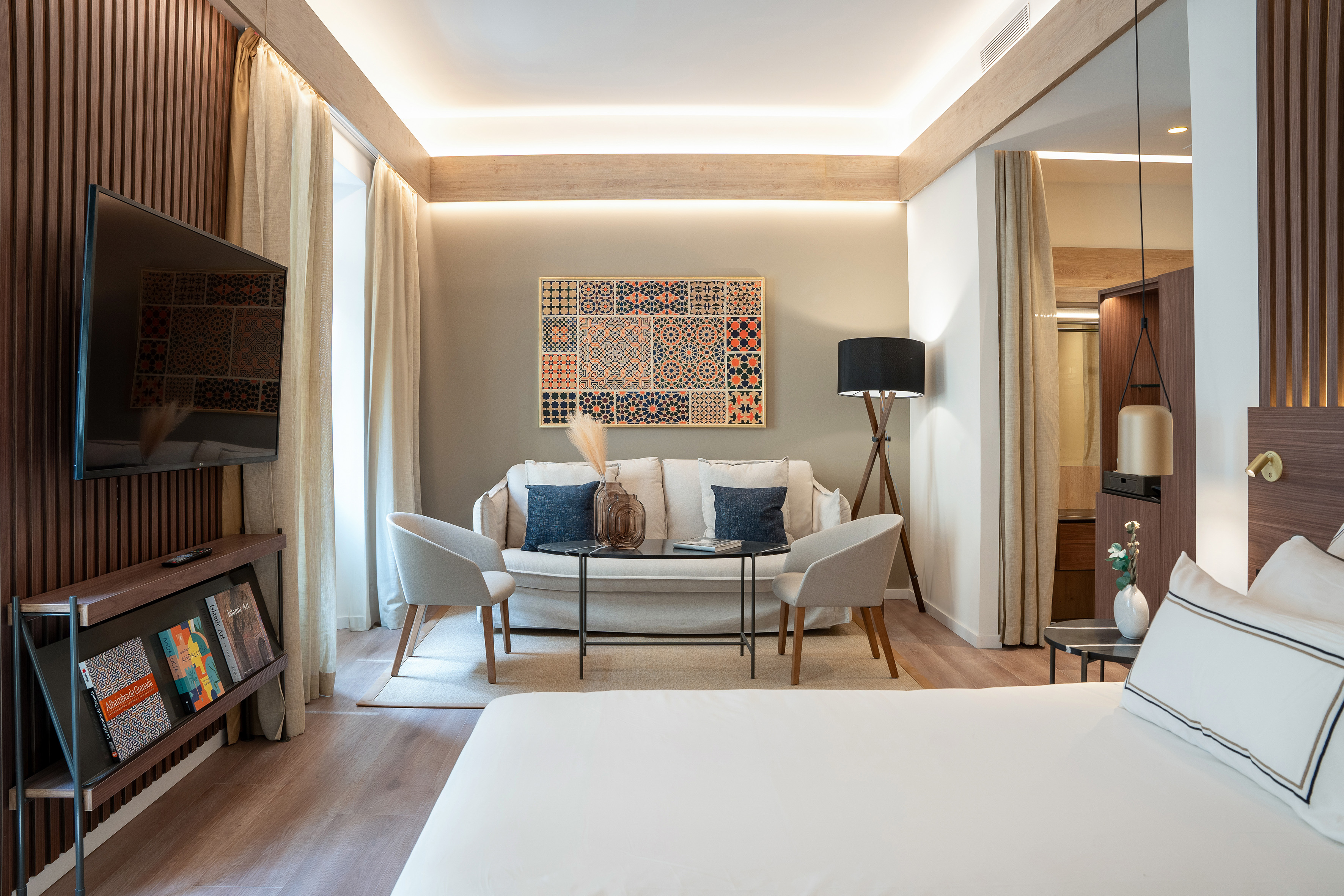 Elegant hotel bedroom and living area with sofa, TV, and patterned art.