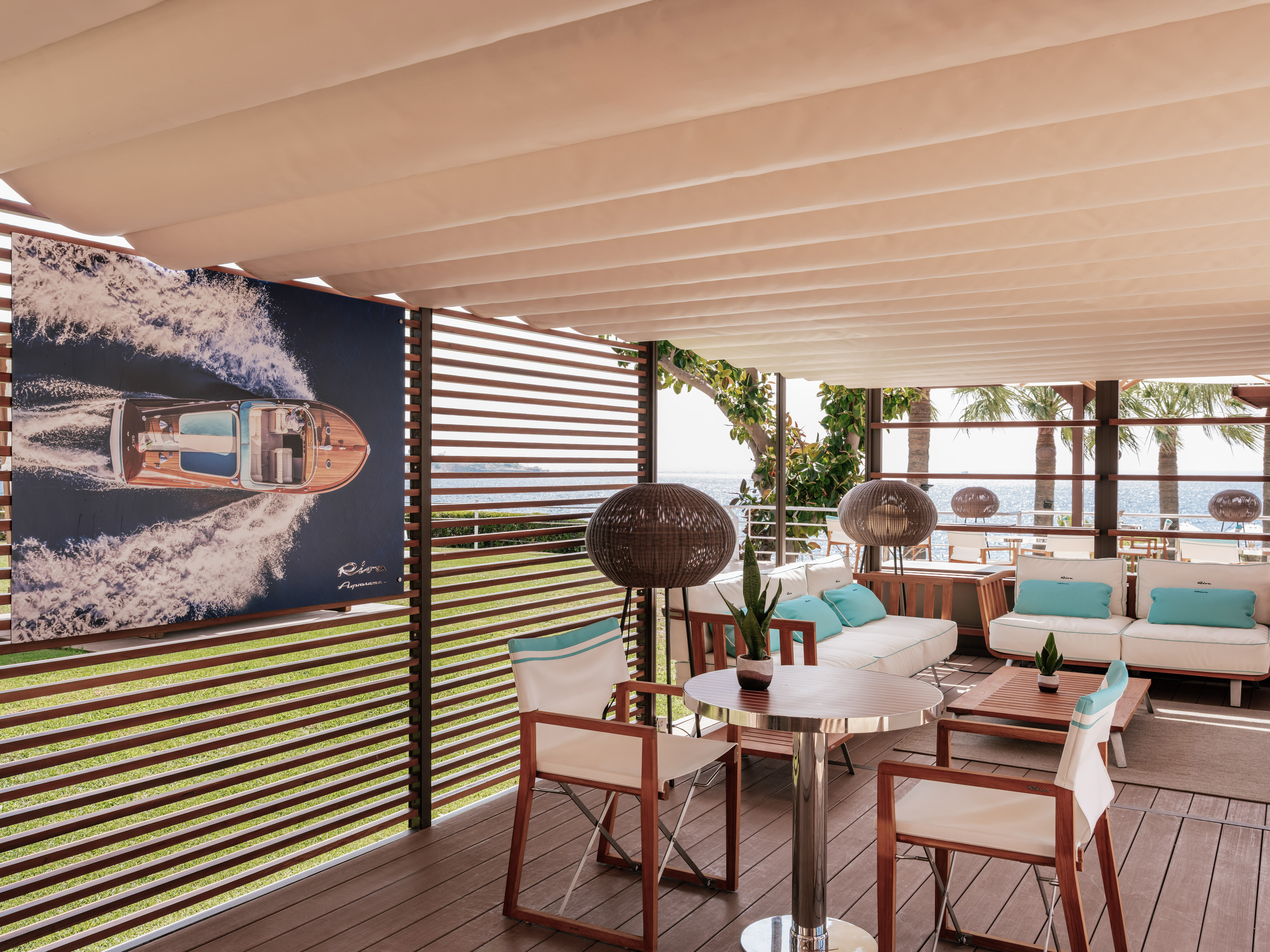 Outdoor lounge patio with wooden deck, boat art, white sofas, and sea view.
