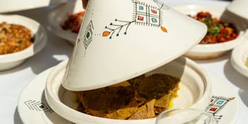 a person holding a tagine over a plate of food