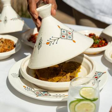 a person holding a tagine over a plate of food