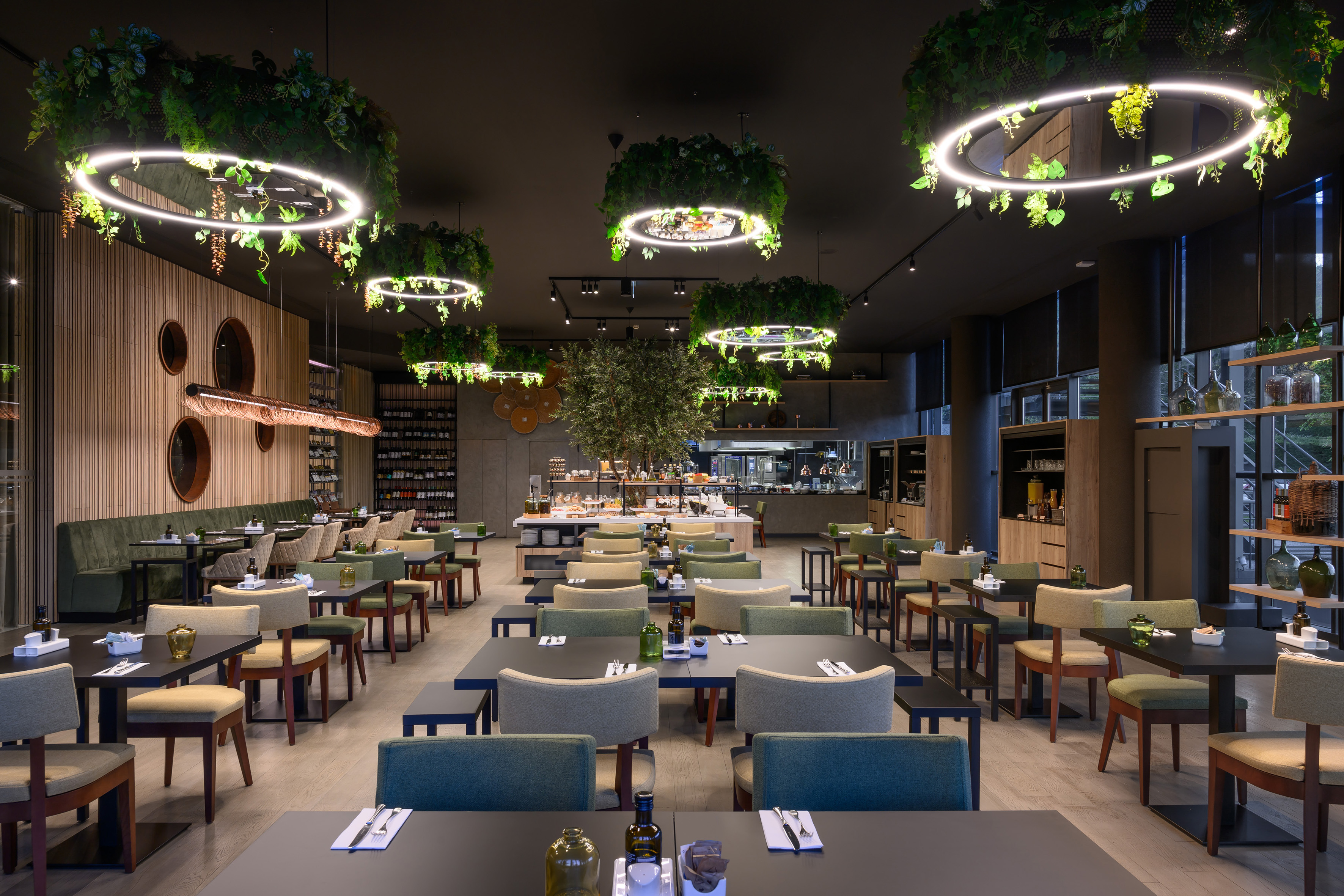 Modern restaurant dining with green chairs, circular plant chandeliers, and buffet.