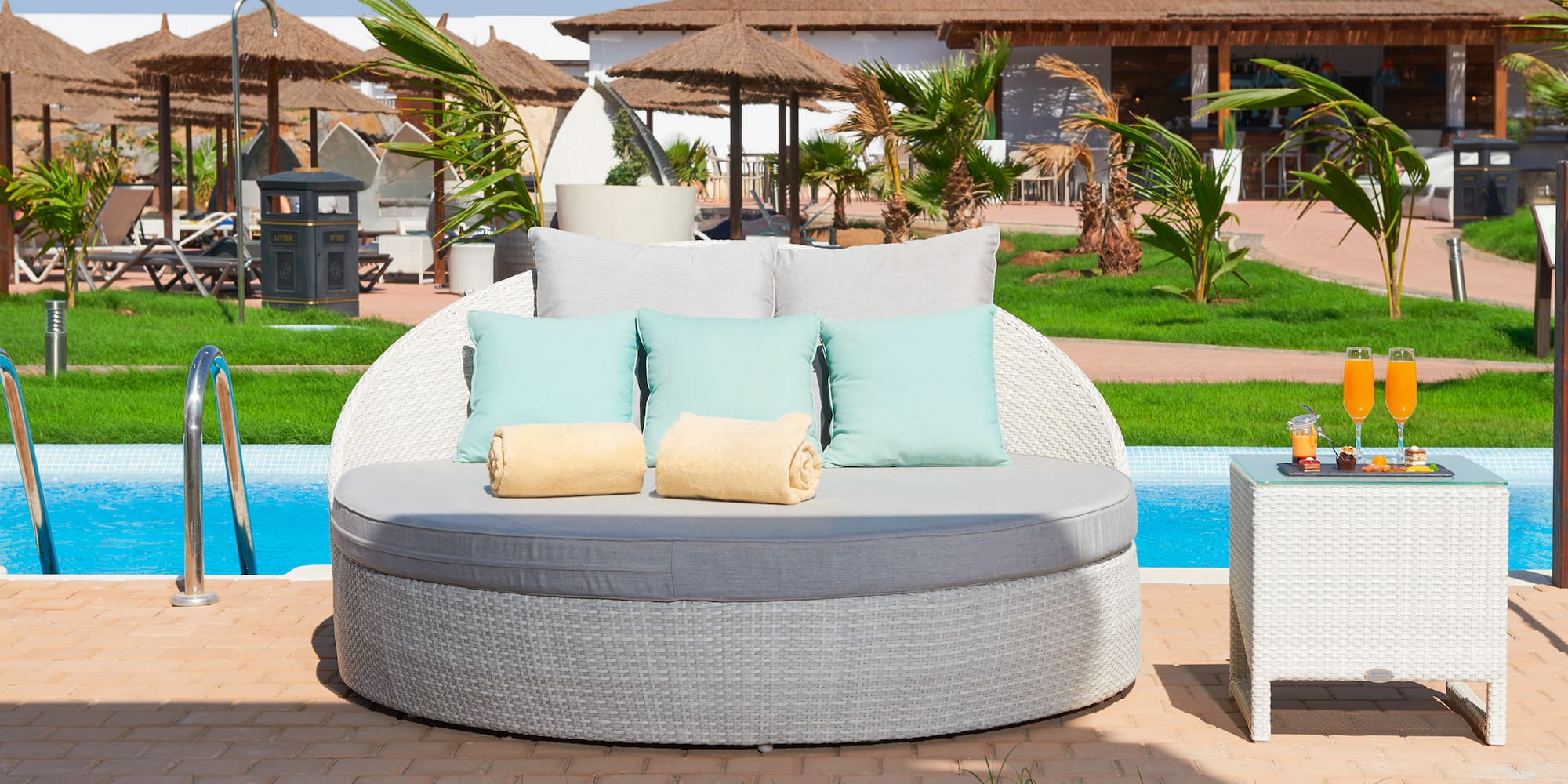 a round white sofa with pillows and a table next to a pool