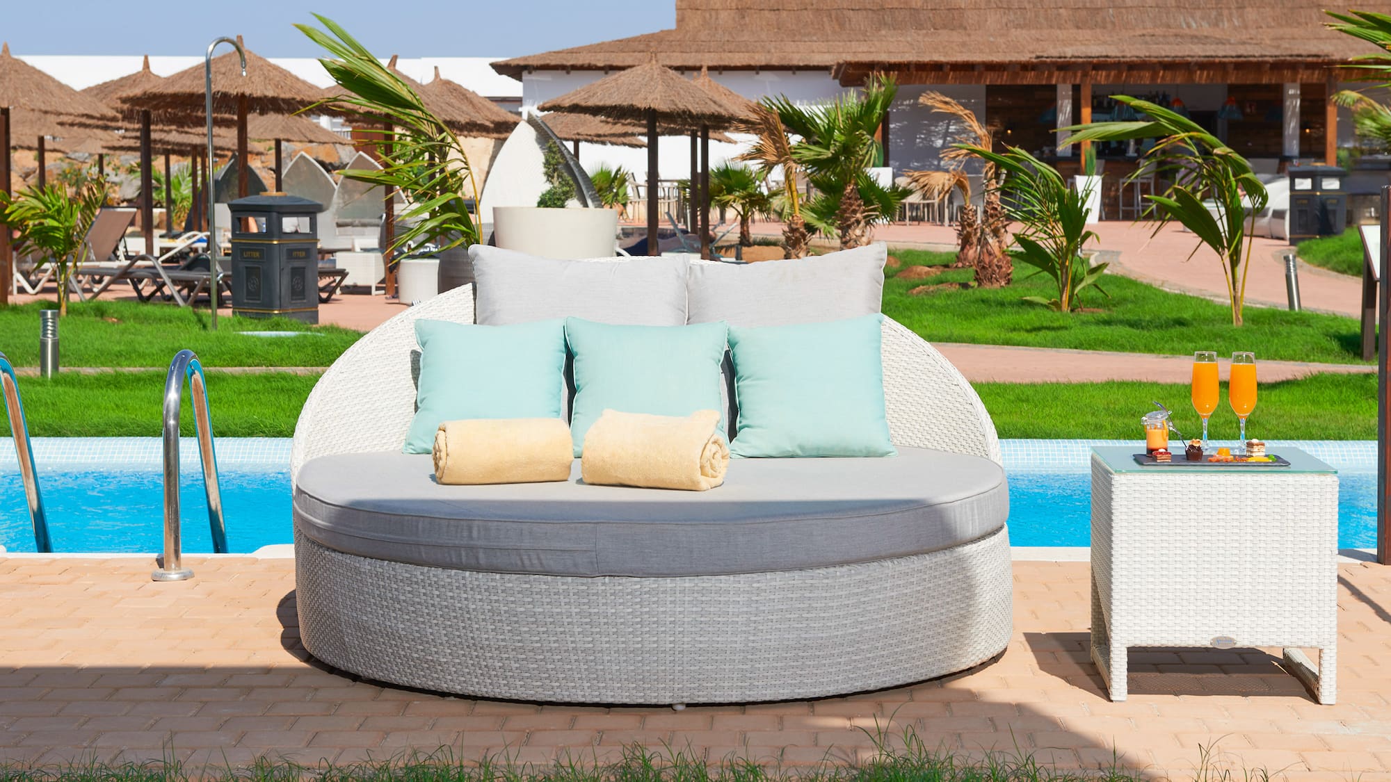 a round white sofa with pillows and a table next to a pool