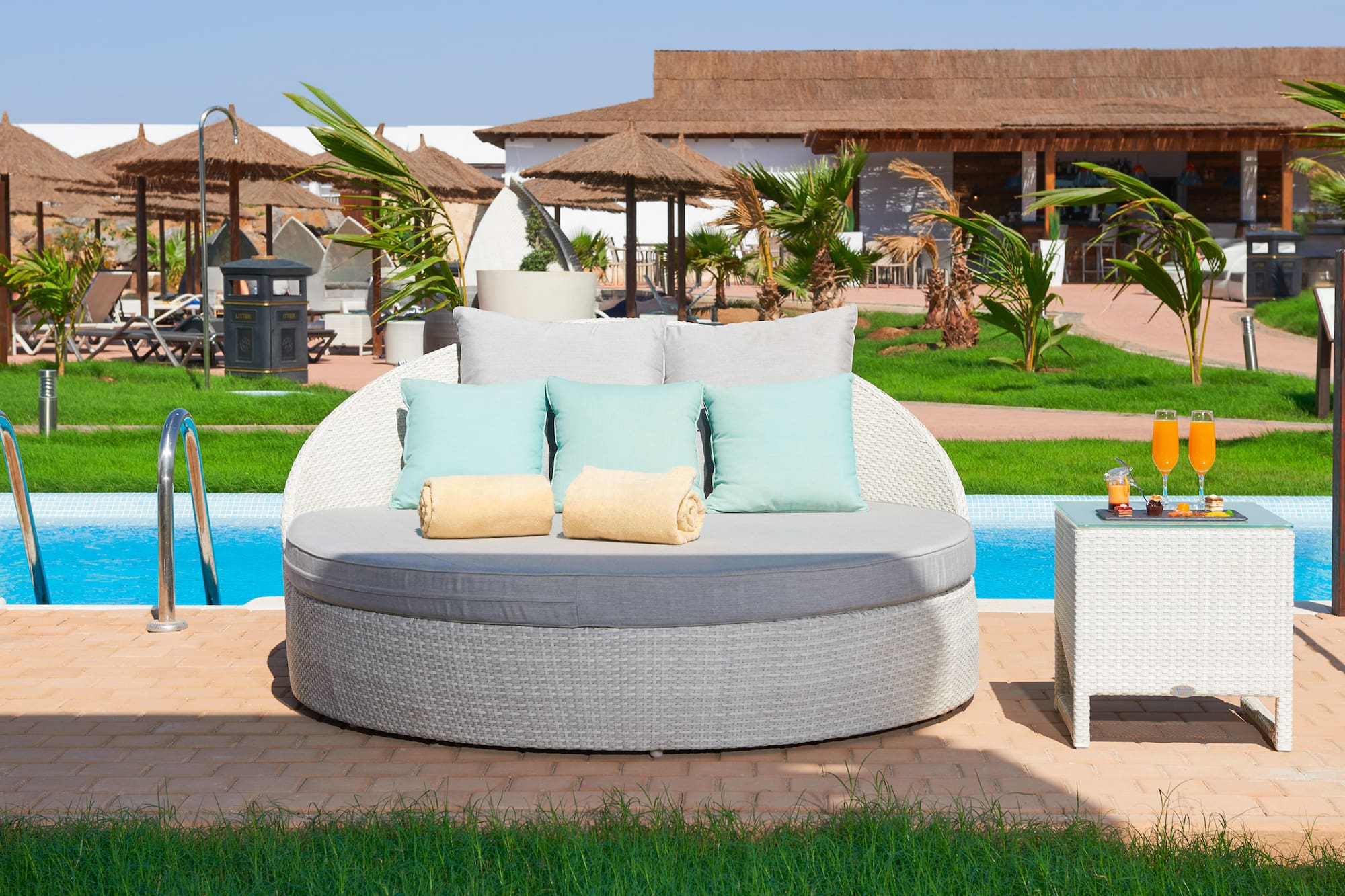 a round white sofa with pillows and a table next to a pool