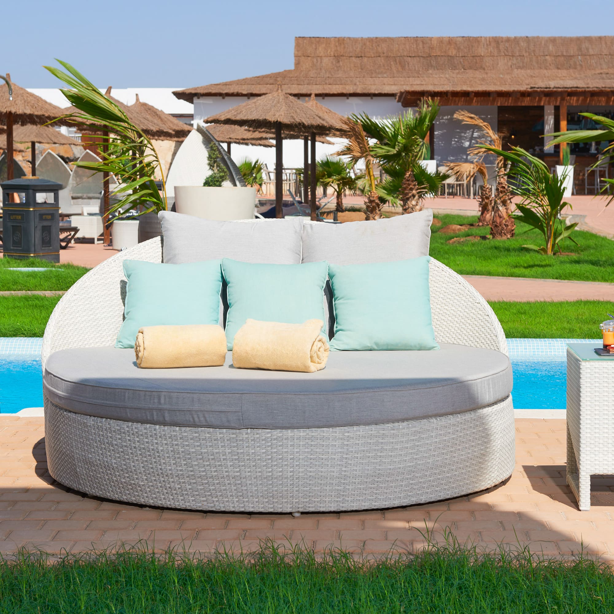 a round white sofa with pillows and a table next to a pool