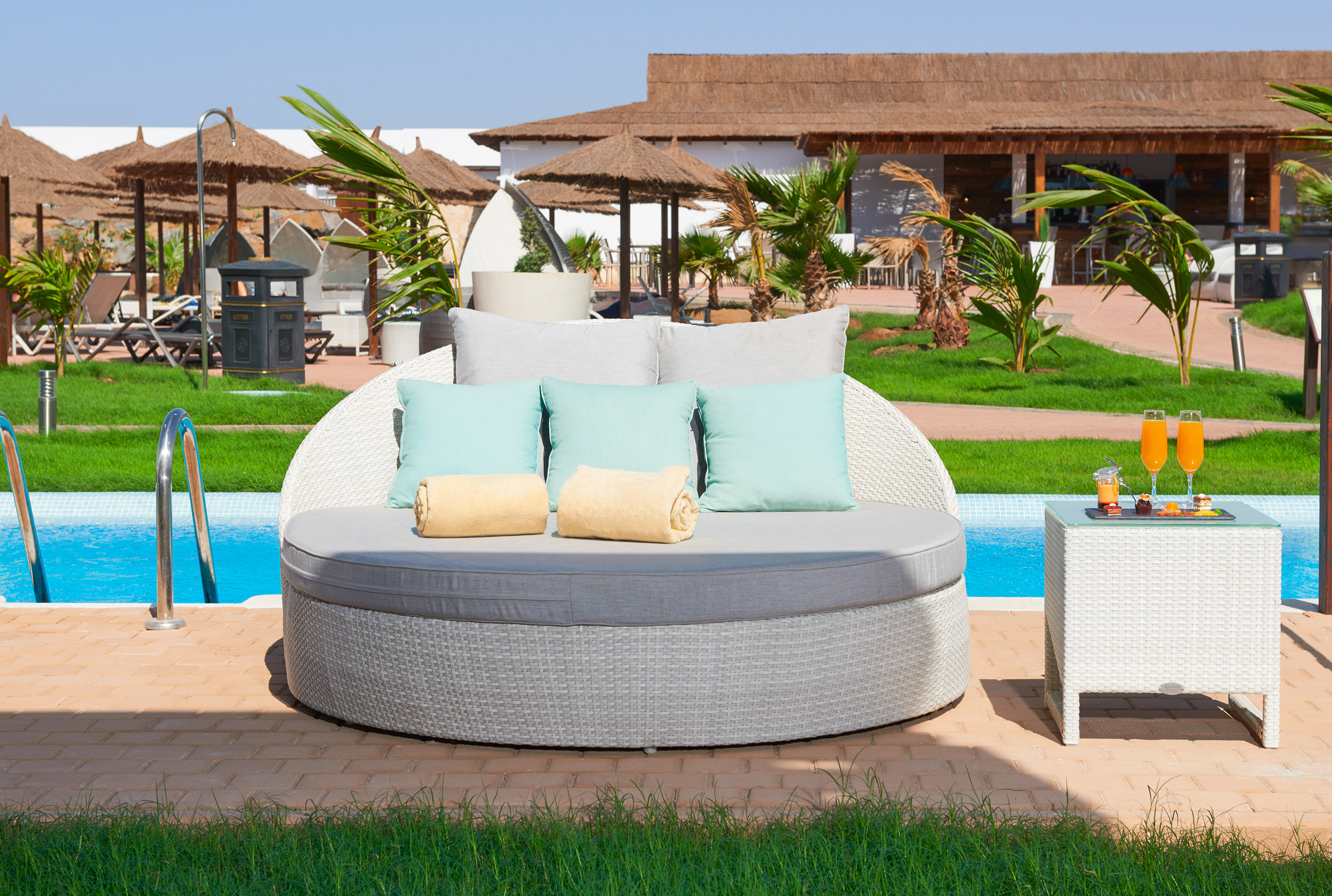 a round white sofa with pillows and a table next to a pool