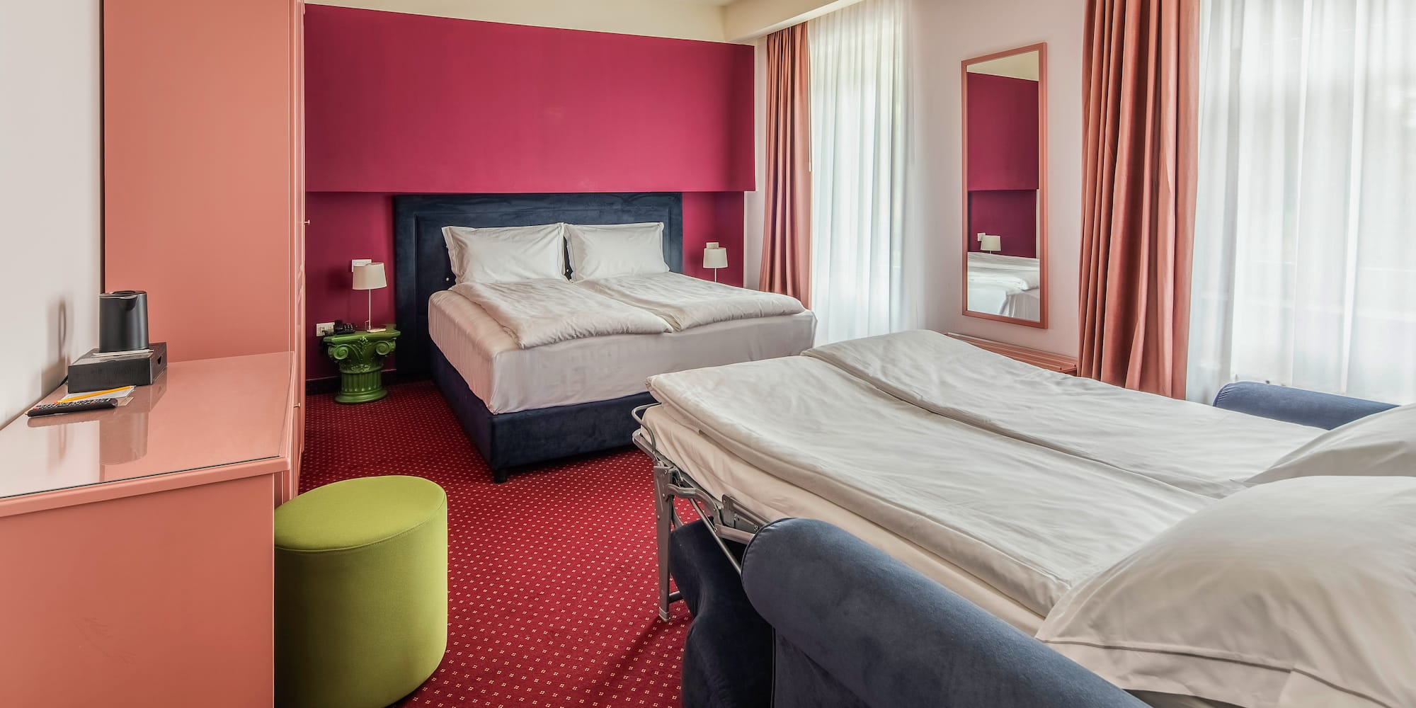 Hotel room with double bed, sofa bed, red accent wall, and red carpet.