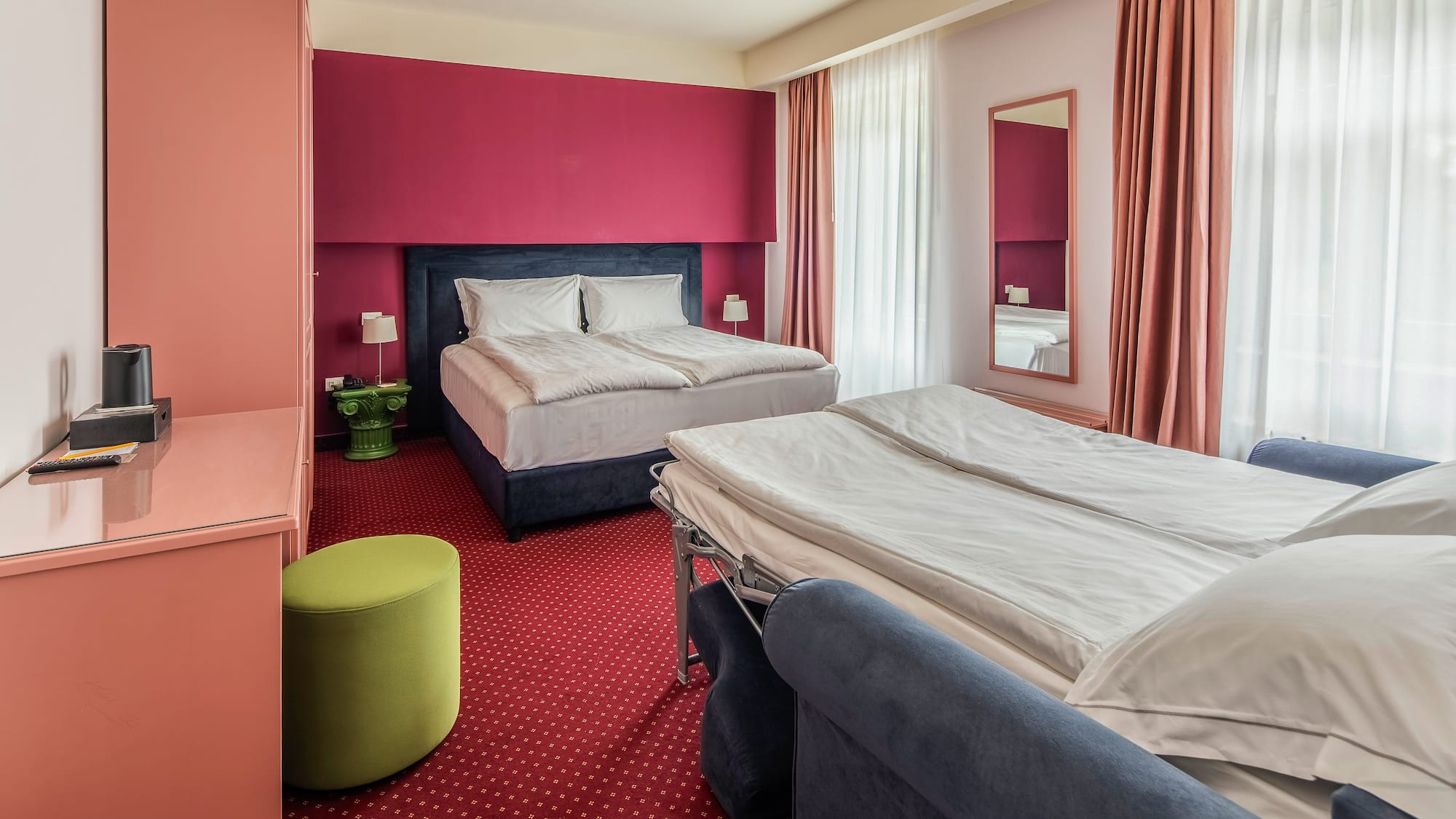 Hotel room with double bed, sofa bed, red accent wall, and red carpet.