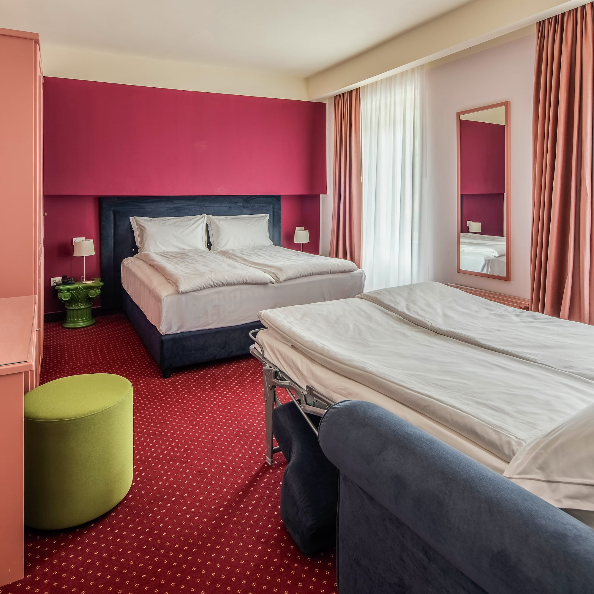 Hotel room with double bed, sofa bed, red accent wall, and red carpet.