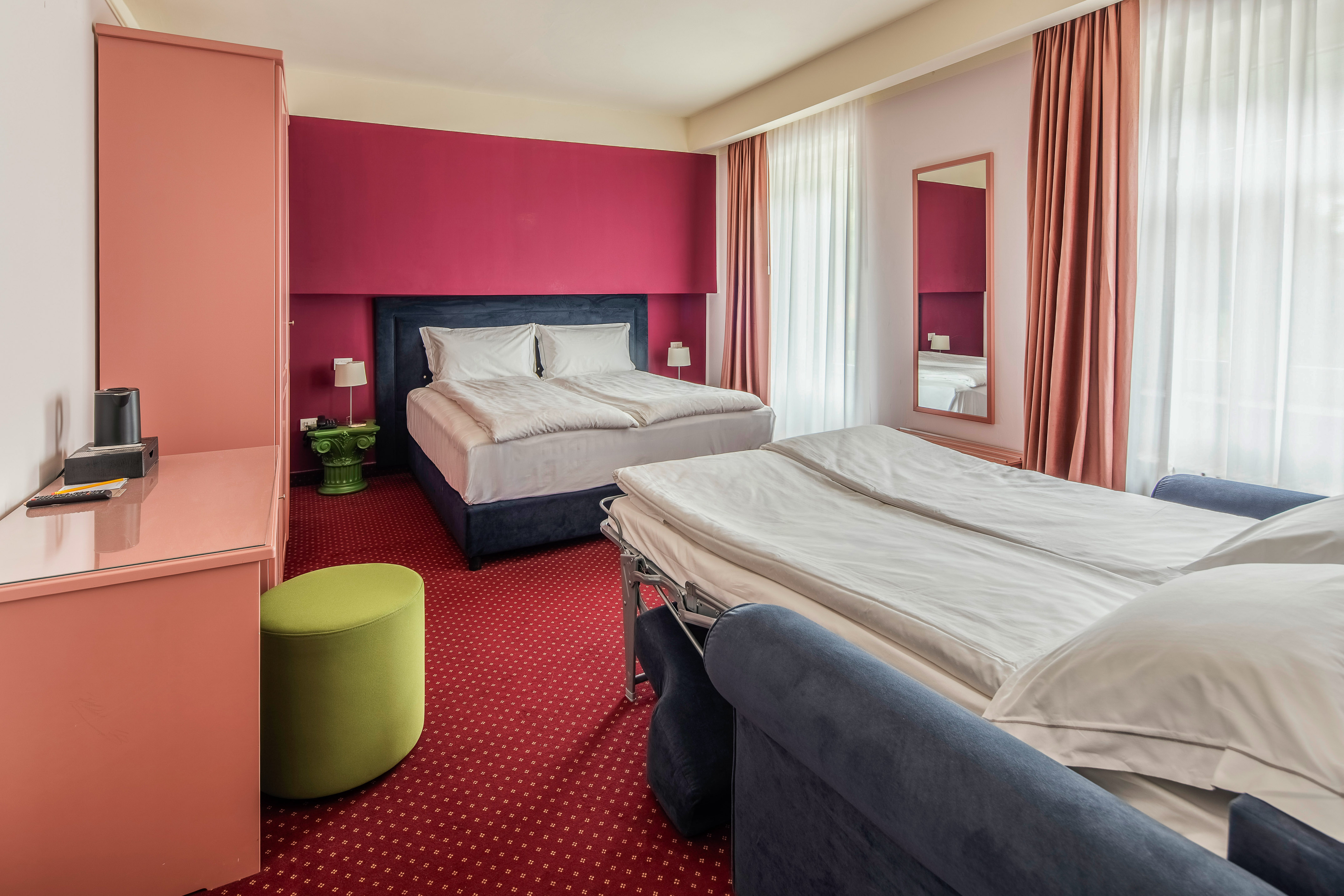 Hotel room with double bed, sofa bed, red accent wall, and red carpet.