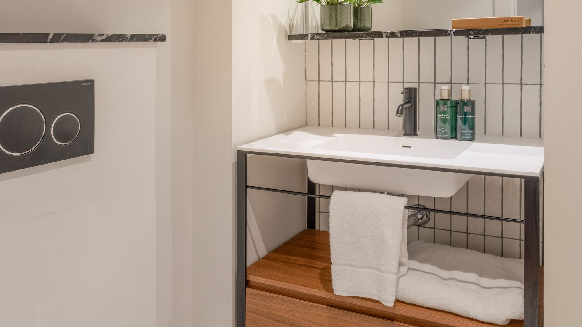 Modern bathroom with white toilet, sink, wooden vanity, mirror, and plant.