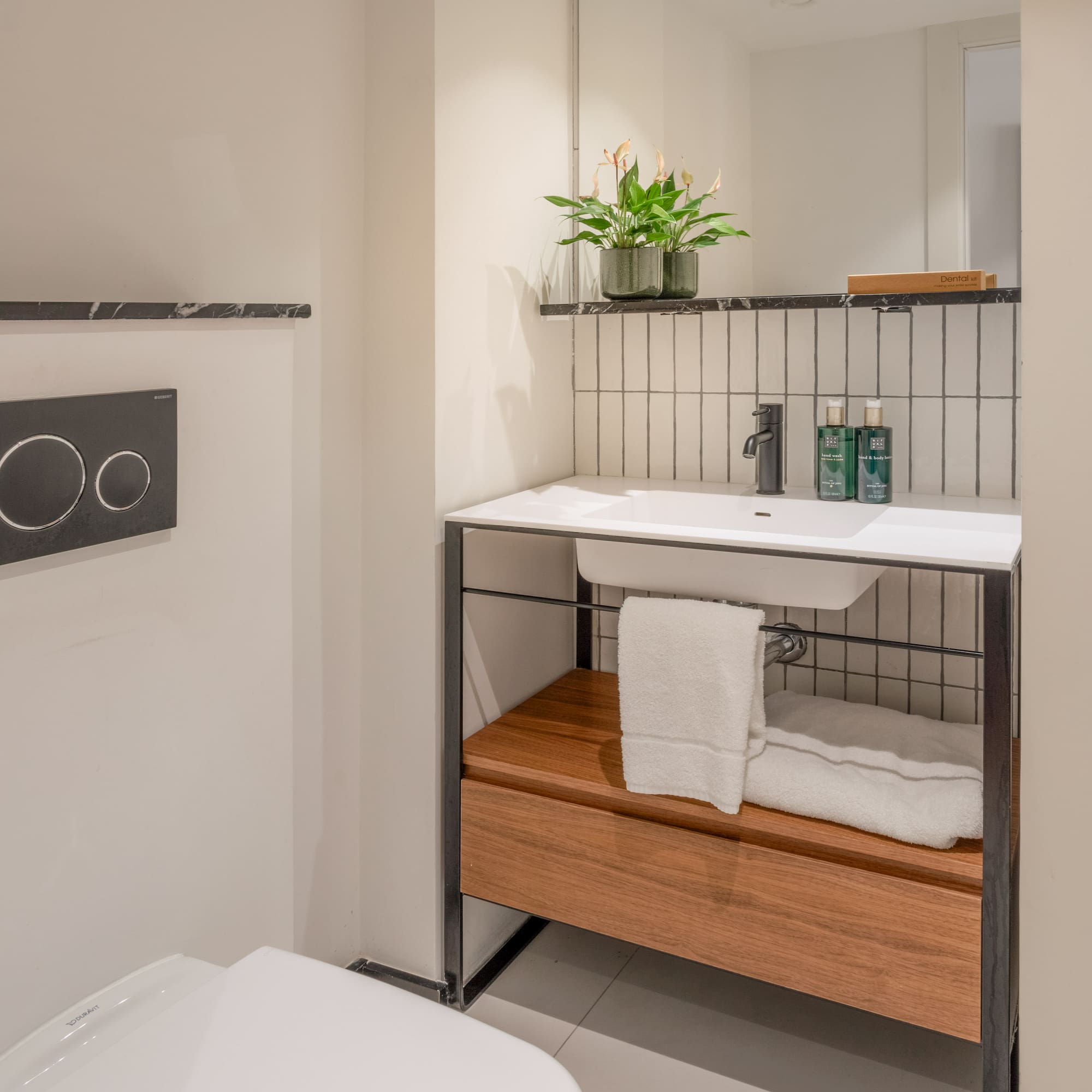 Modern bathroom with white toilet, sink, wooden vanity, mirror, and plant.