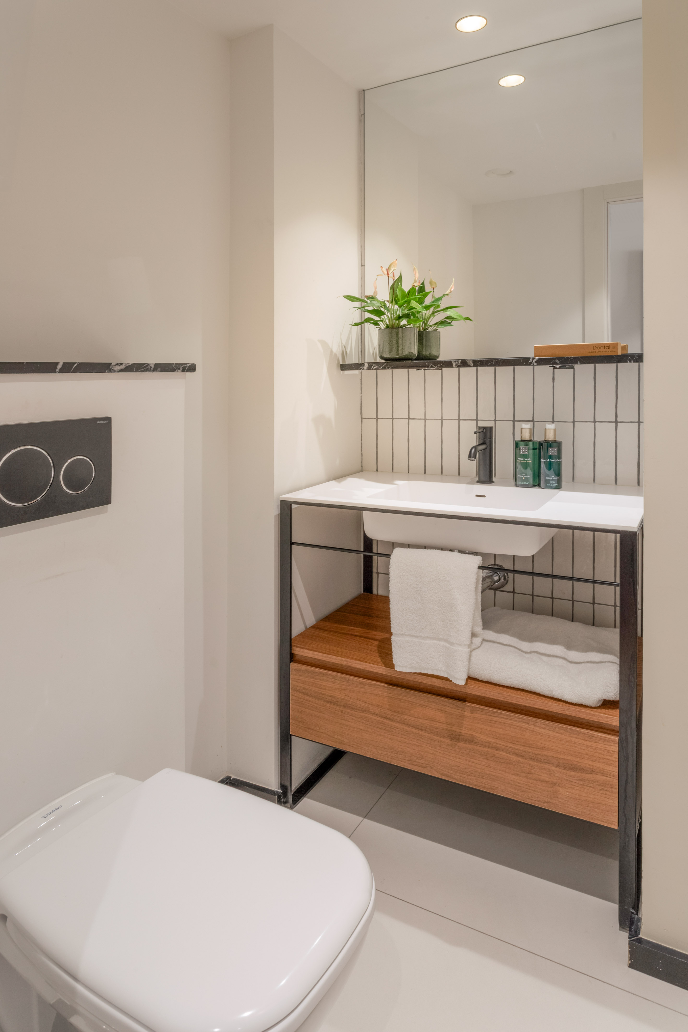 Modern bathroom with white toilet, sink, wooden vanity, mirror, and plant.
