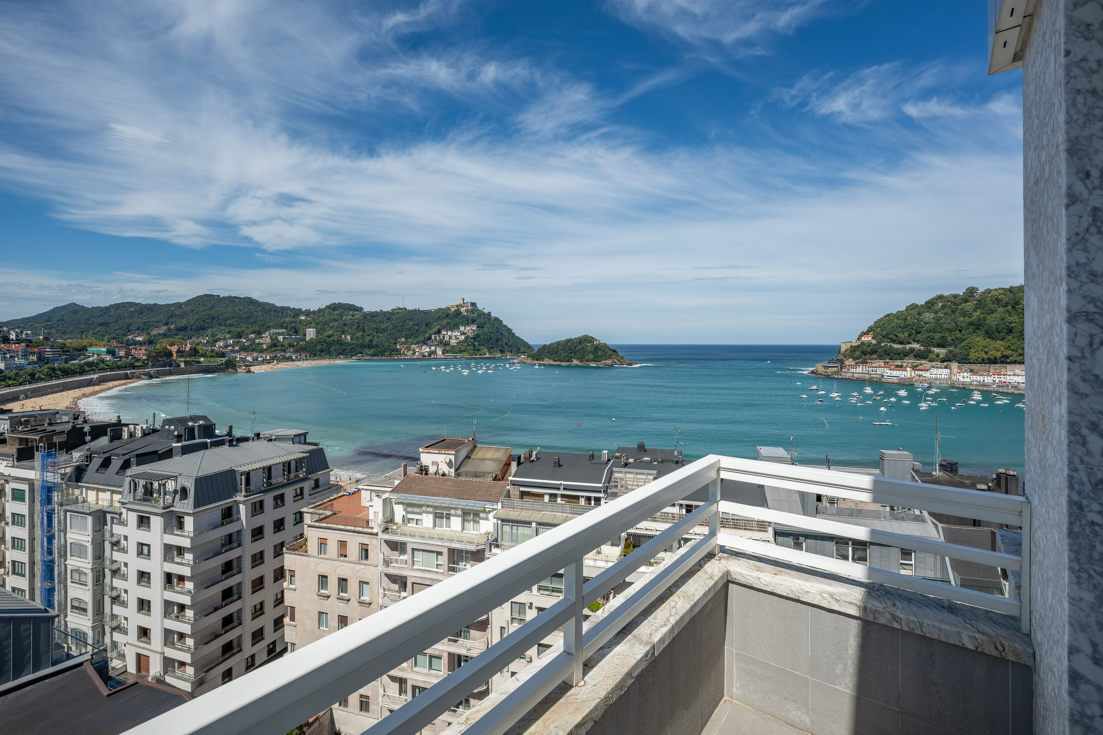 Balcony view of San Sebastian's La Concha Bay, beach, island, and city.