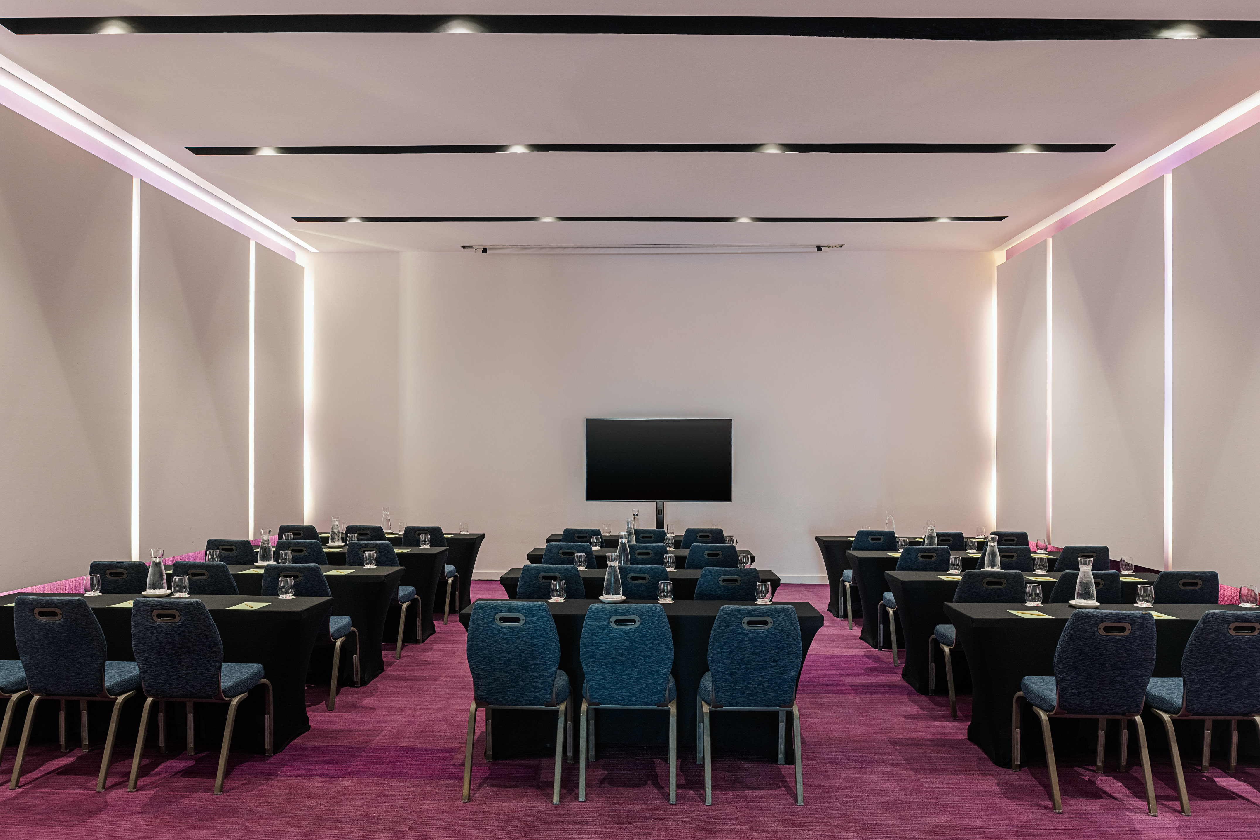 Empty modern meeting room with blue chairs, black tables, purple carpet, and TV.