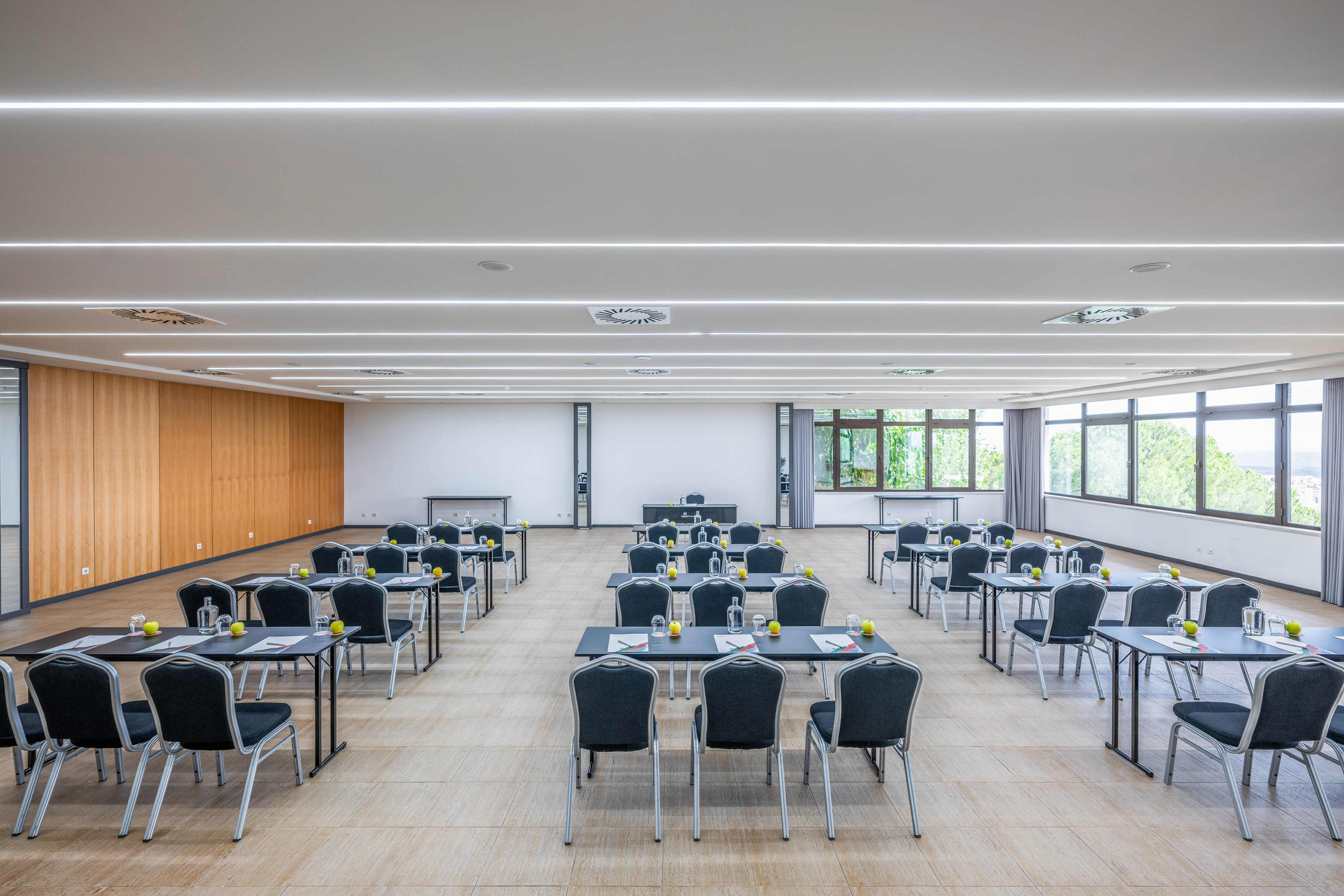 Modern conference room classroom setup with tables, chairs, bright windows.