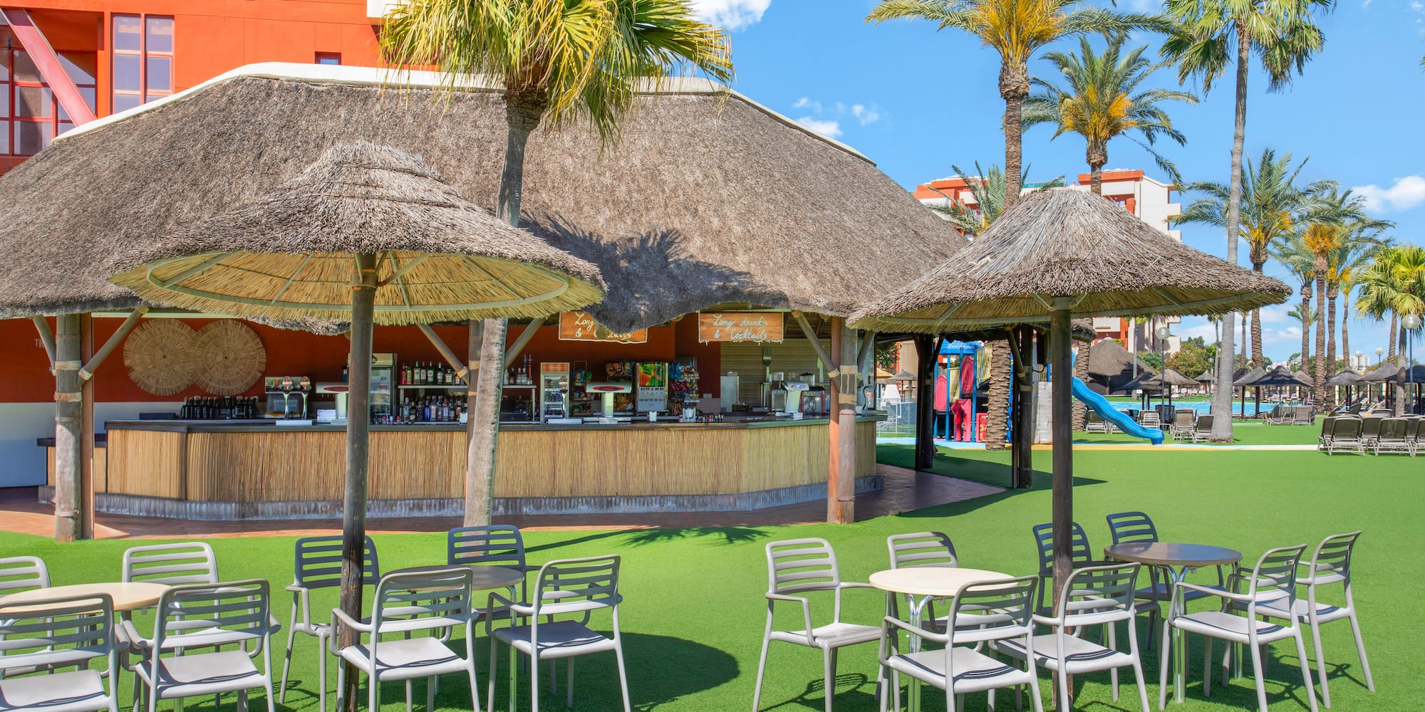 Tropical poolside bar with thatched roof, outdoor seating, and palm trees.
