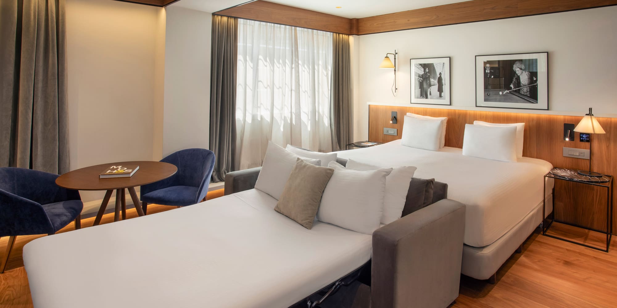 Hotel room with bed, unfolded sofa bed, and a table with blue chairs.