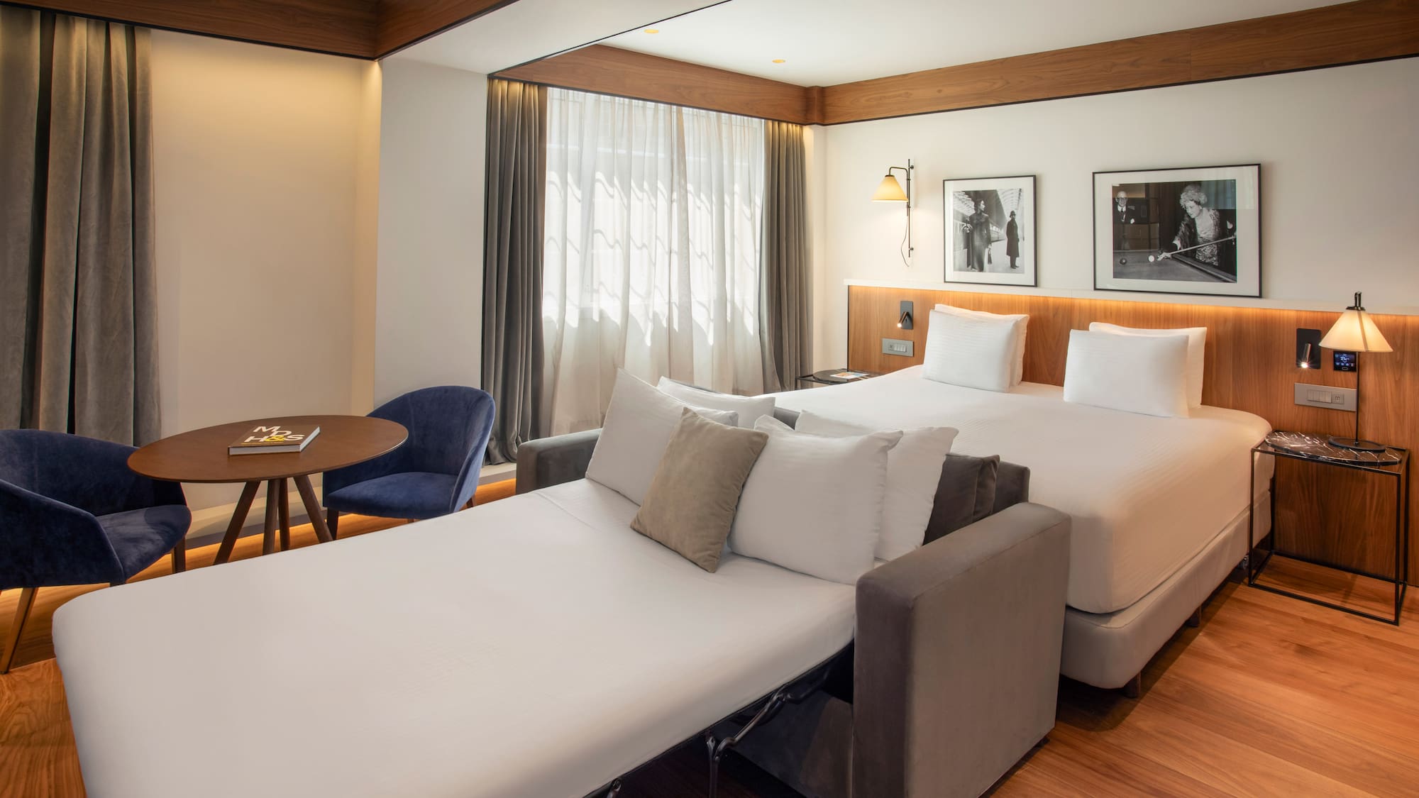 Modern hotel room with bed, pull-out sofa bed, and wooden floor living area.