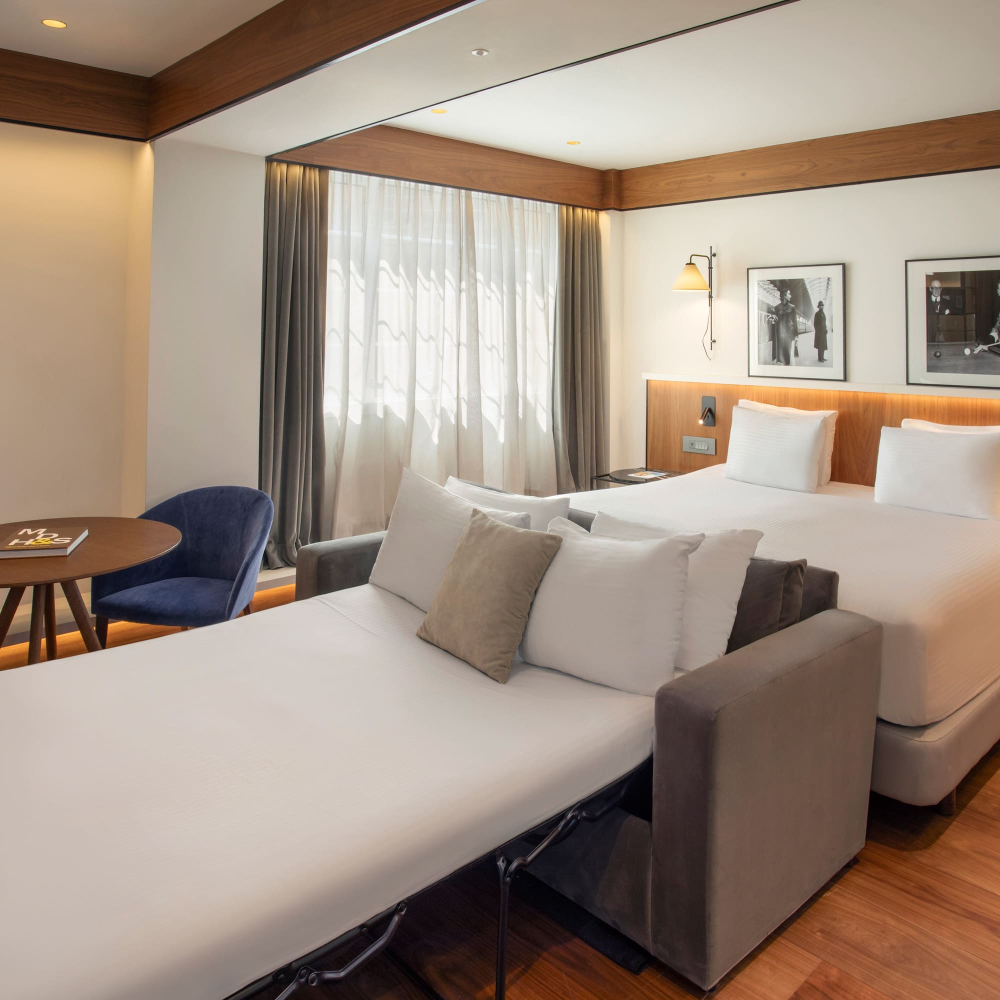 Hotel room with bed, unfolded sofa bed, and a table with blue chairs.