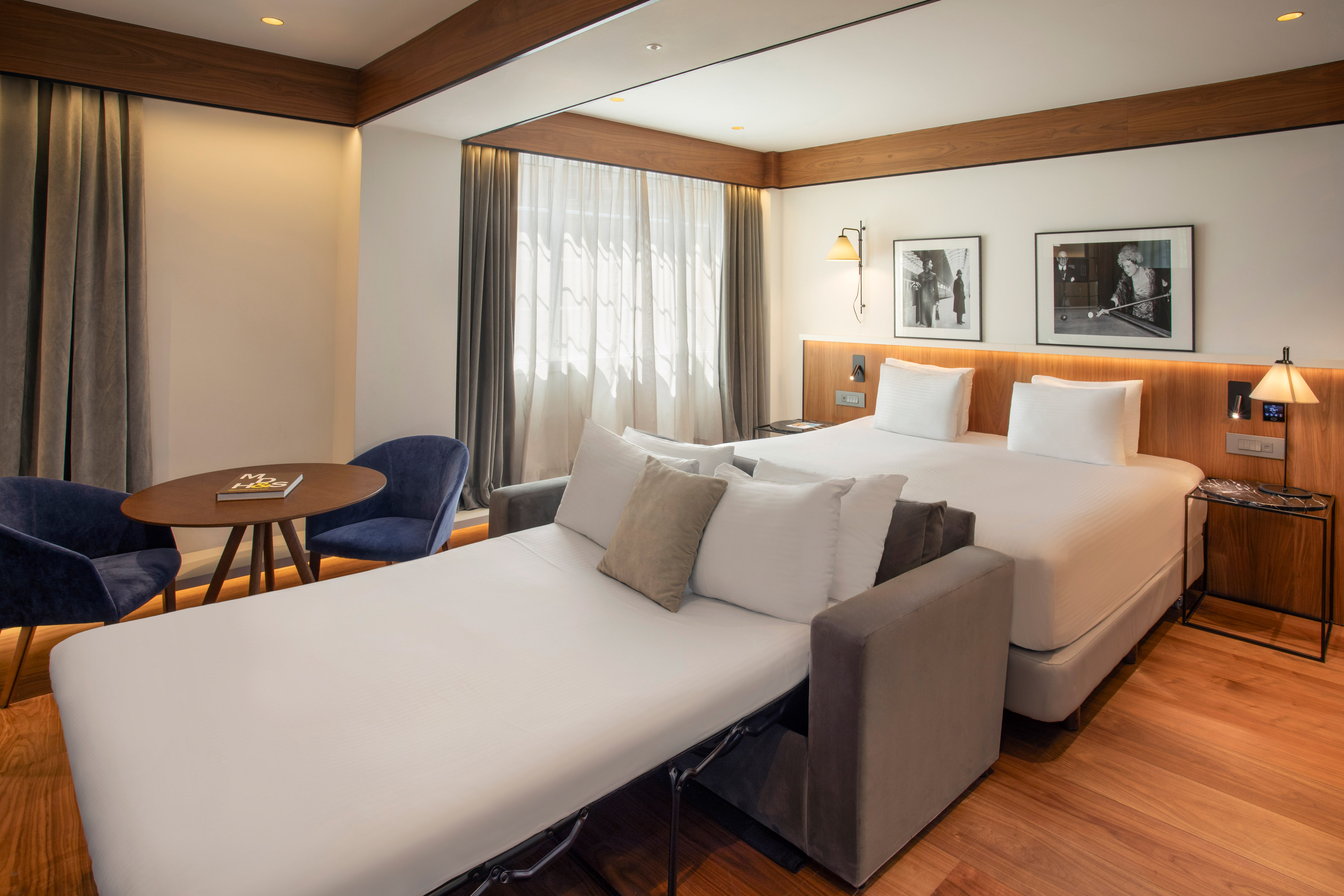 Hotel room with bed, unfolded sofa bed, and a table with blue chairs.