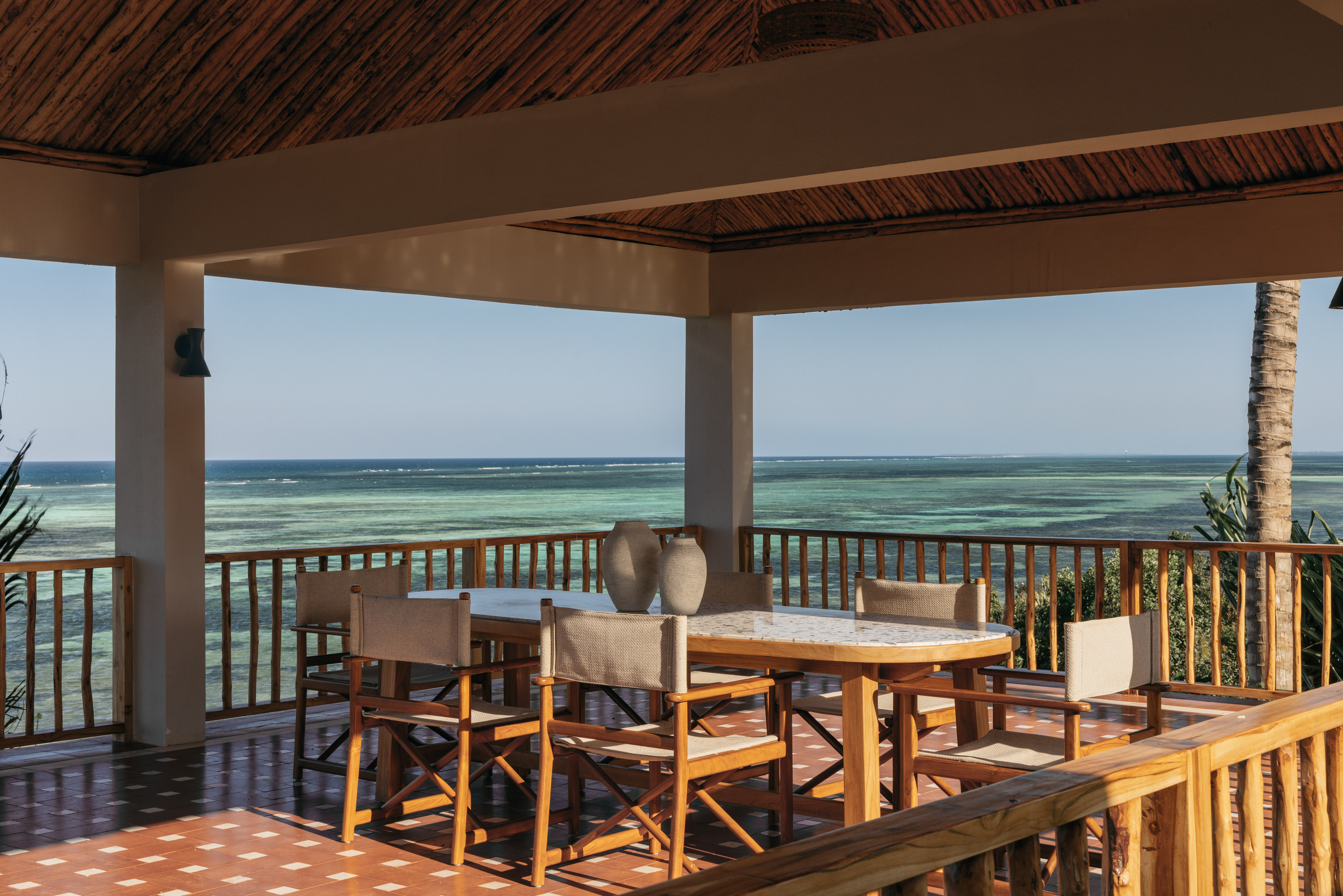 Beachfront patio with wooden dining table, chairs, and expansive ocean view.