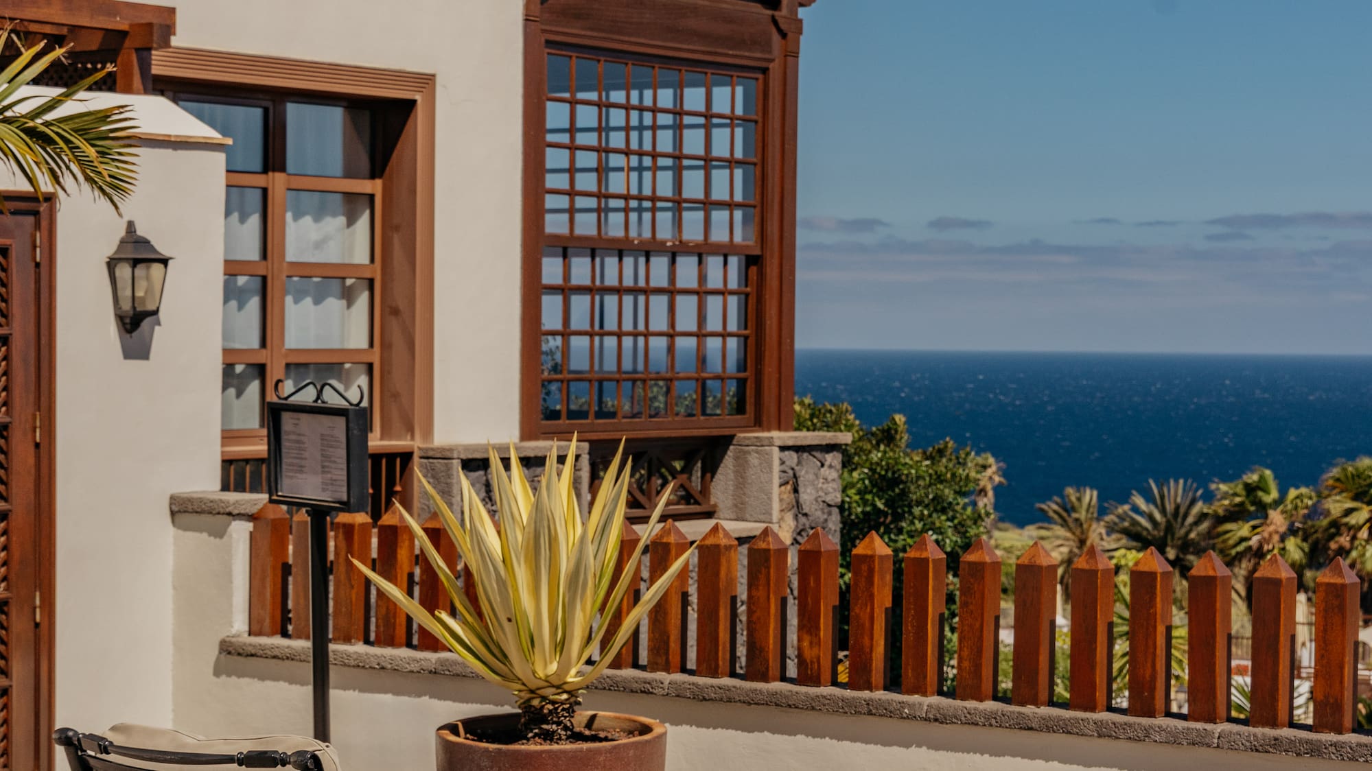 Sunny resort patio with lounge chairs, agave plant, and sea view.