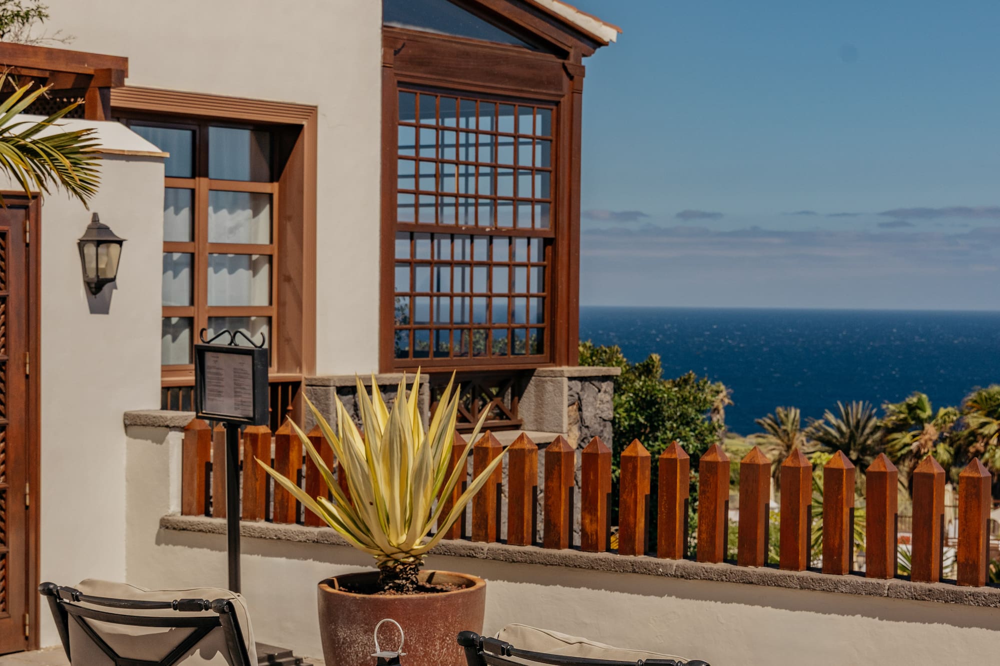 Sunny resort patio with lounge chairs, agave plant, and sea view.