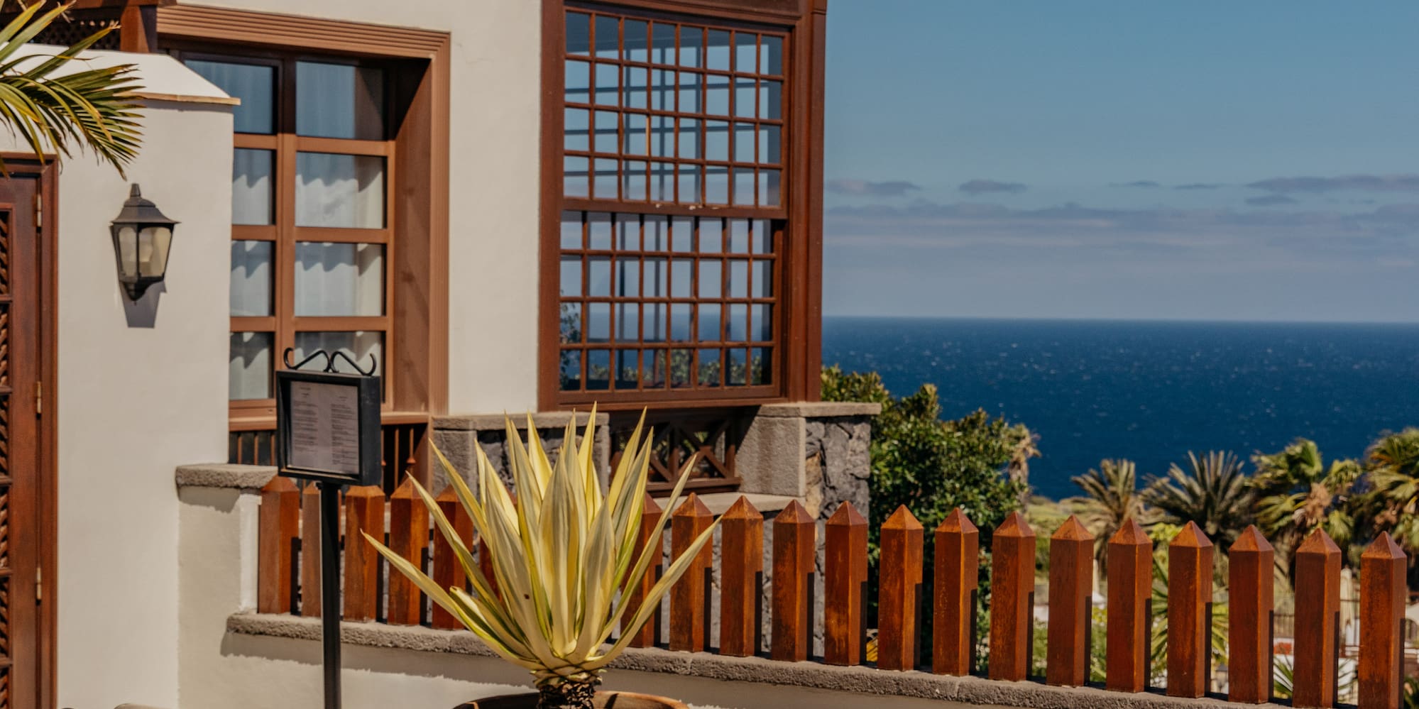 Sunny resort patio with lounge chairs, agave plant, and sea view.
