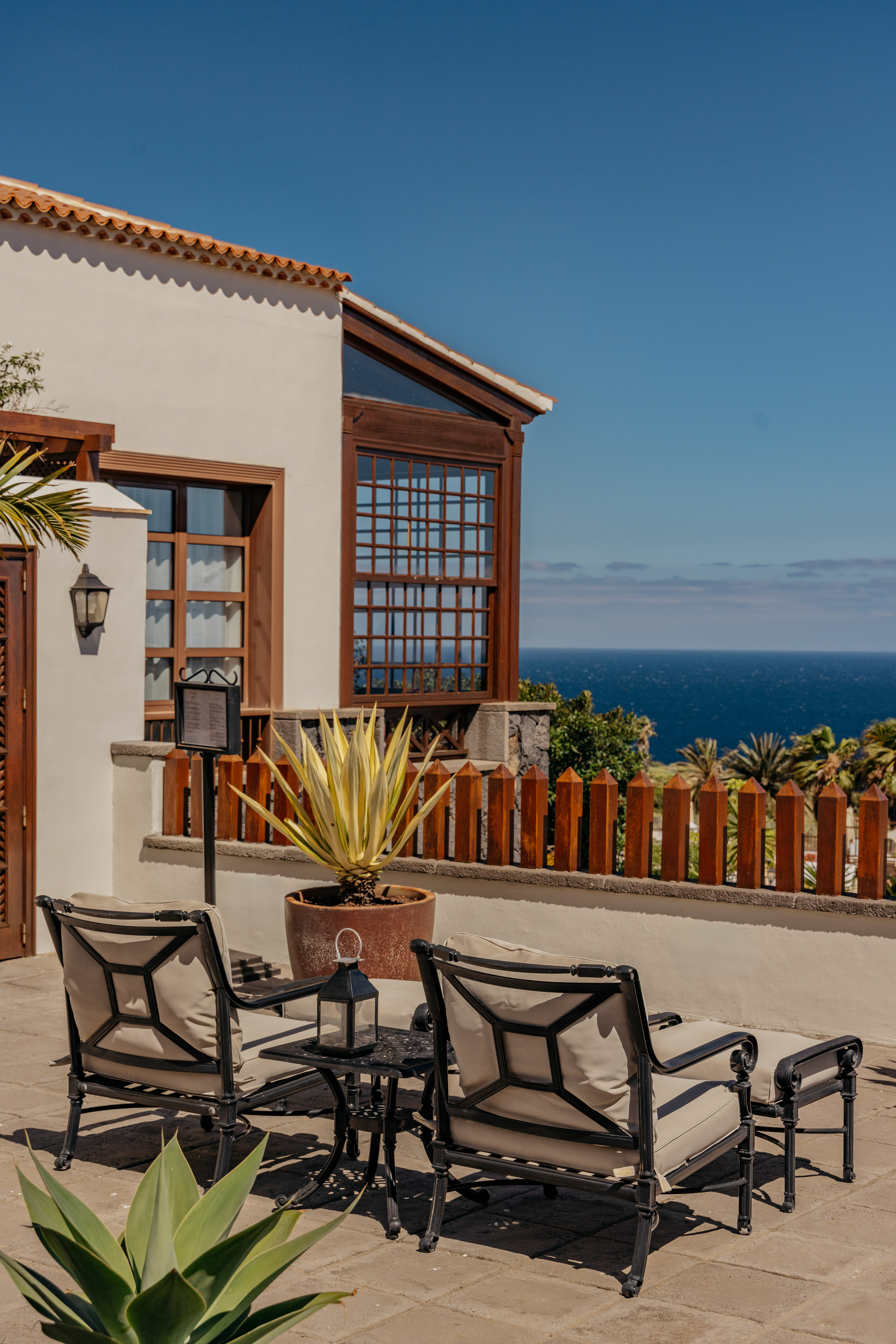 Sunny resort patio with lounge chairs, agave plant, and sea view.