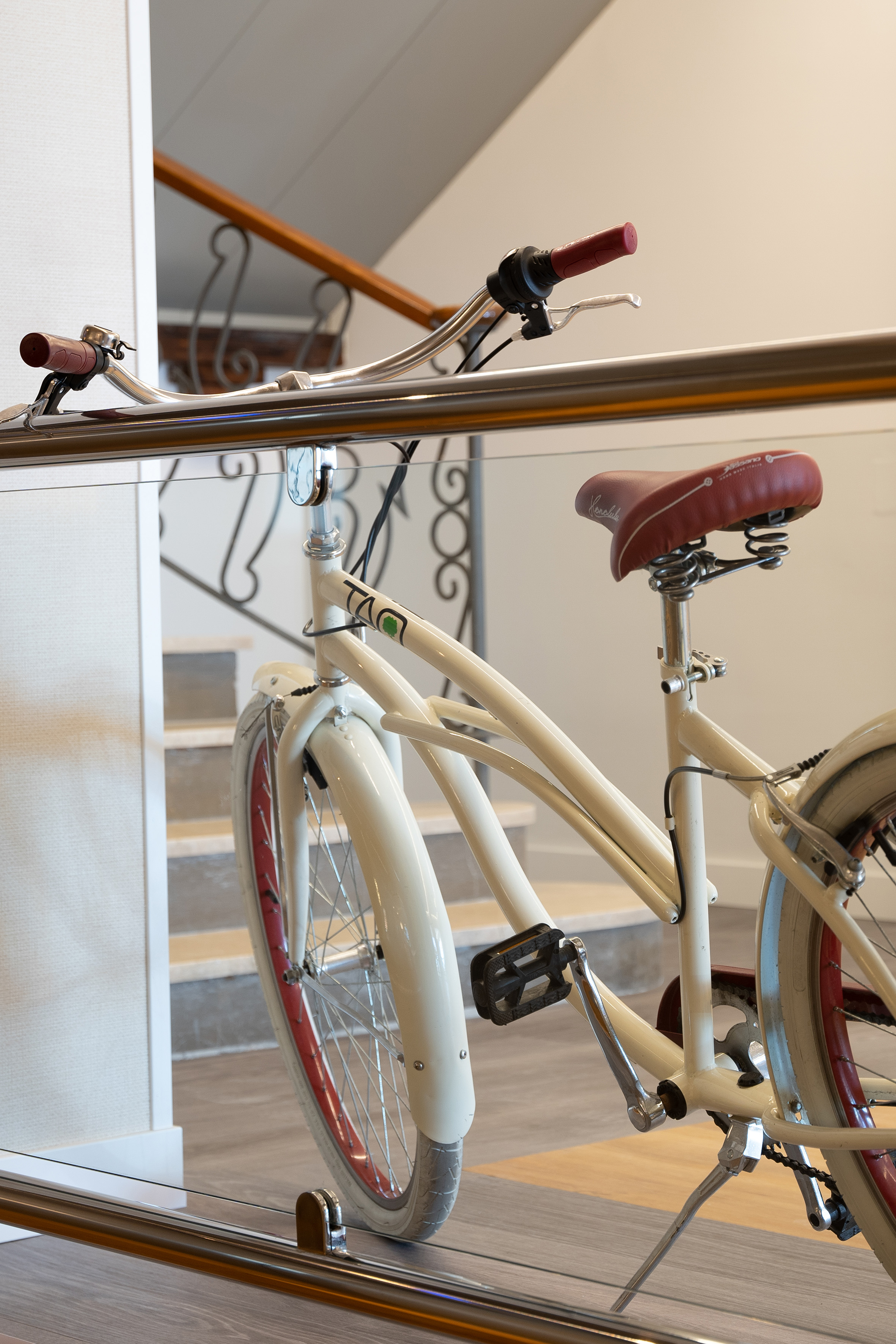 Cream vintage bicycle with red seat, red rims, and bell by indoor staircase.