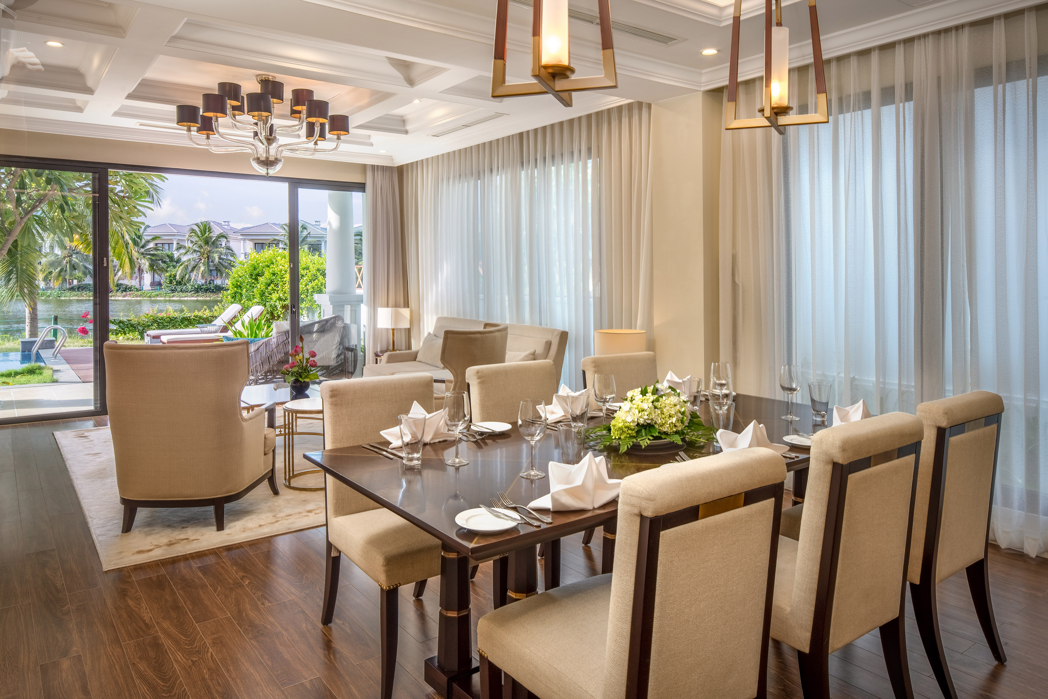 Elegant dining room with set table, modern chandelier, and tropical outdoor view.