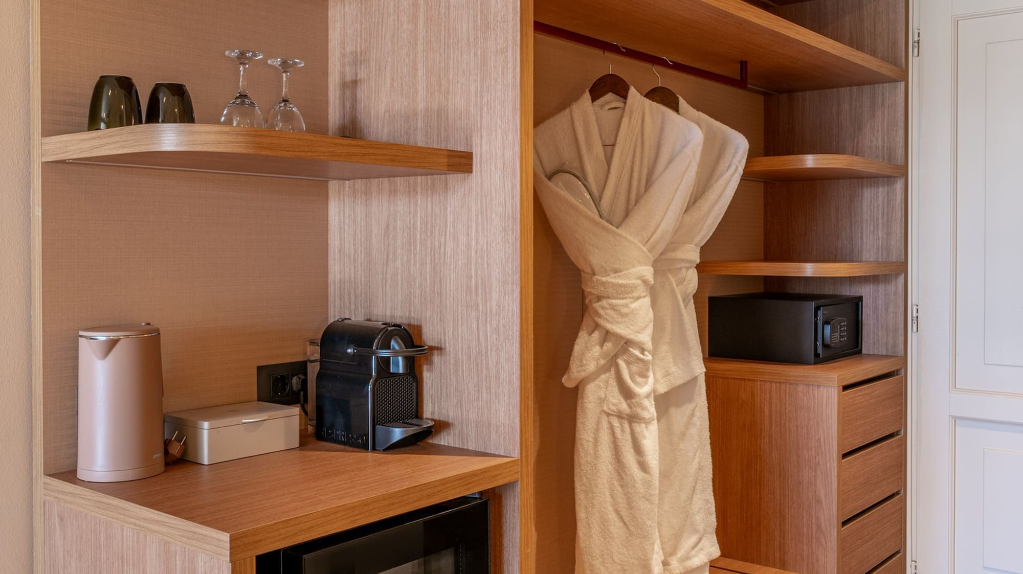 Modern hotel wardrobe with mini-bar, Nespresso, safe, and bathrobes.