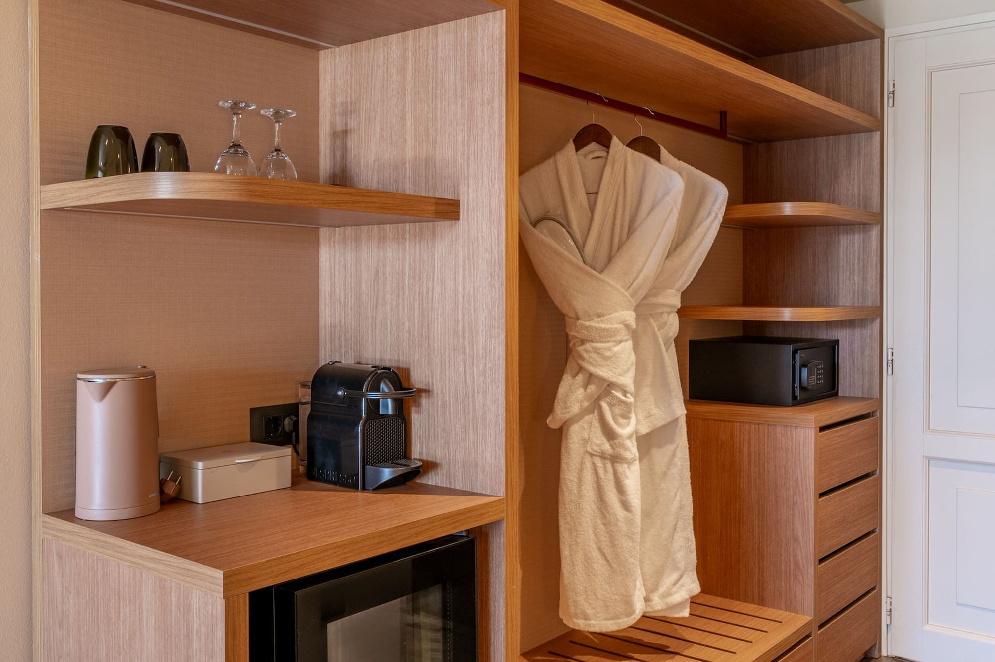 Modern hotel wardrobe with mini-bar, Nespresso, safe, and bathrobes.