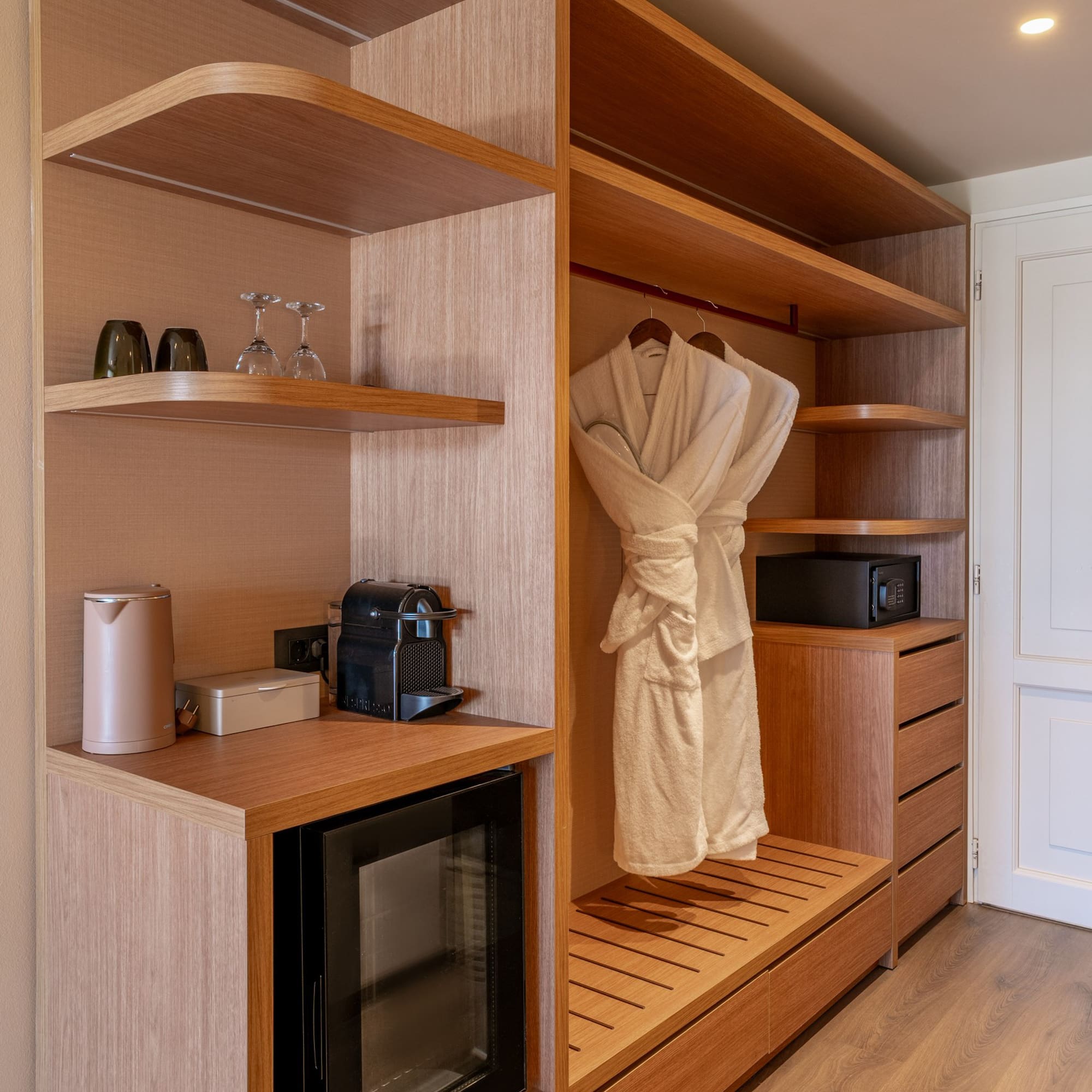 Modern hotel wardrobe with mini-bar, Nespresso, safe, and bathrobes.