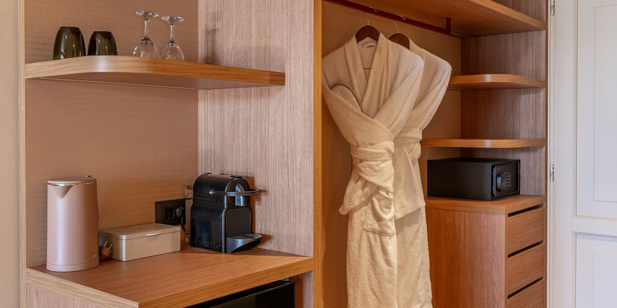 Modern hotel wardrobe with mini-bar, Nespresso, safe, and bathrobes.